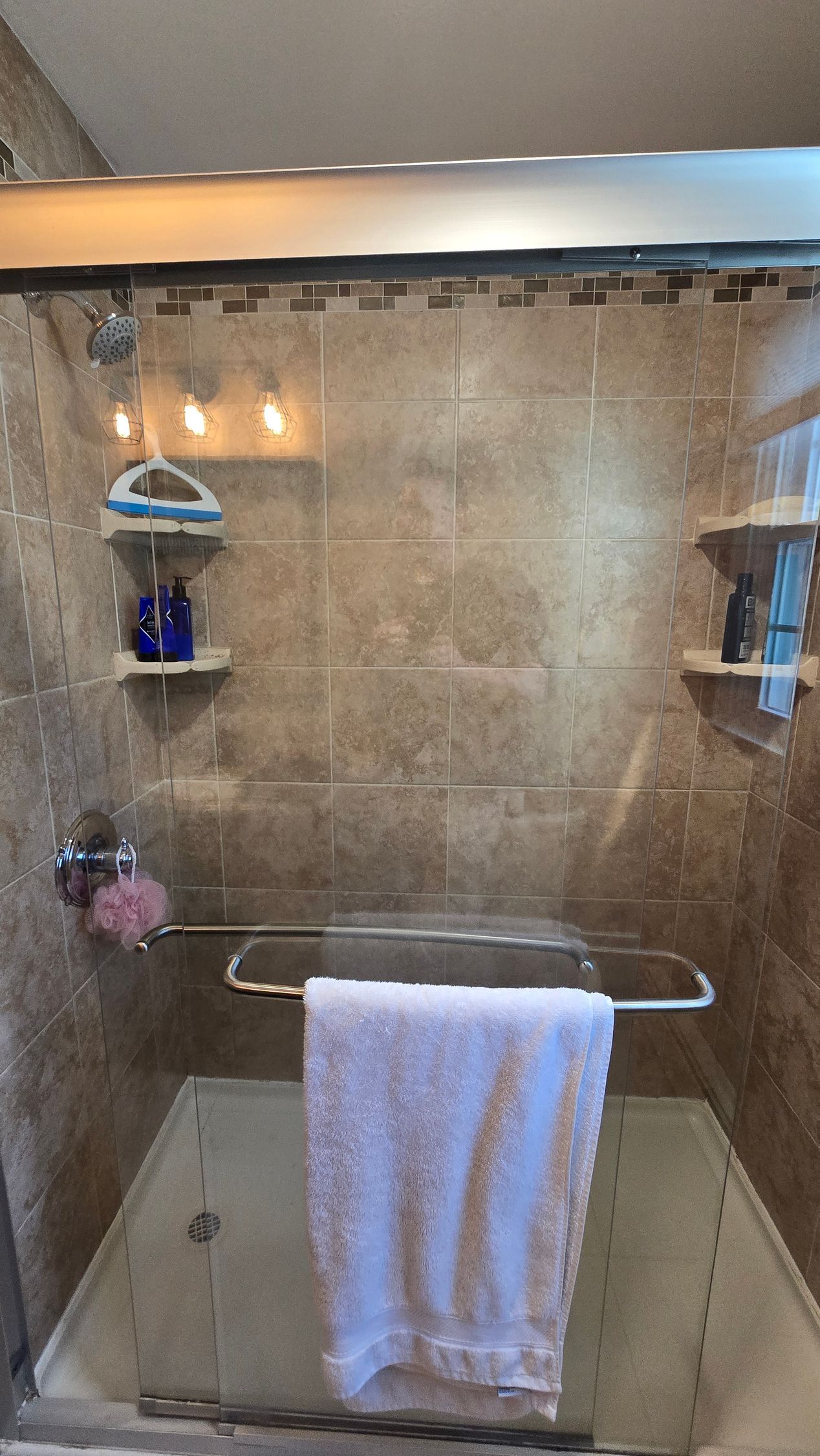 Shower interior with a towel hanging, shelves with toiletries, and beige tiles in Plainville, CT