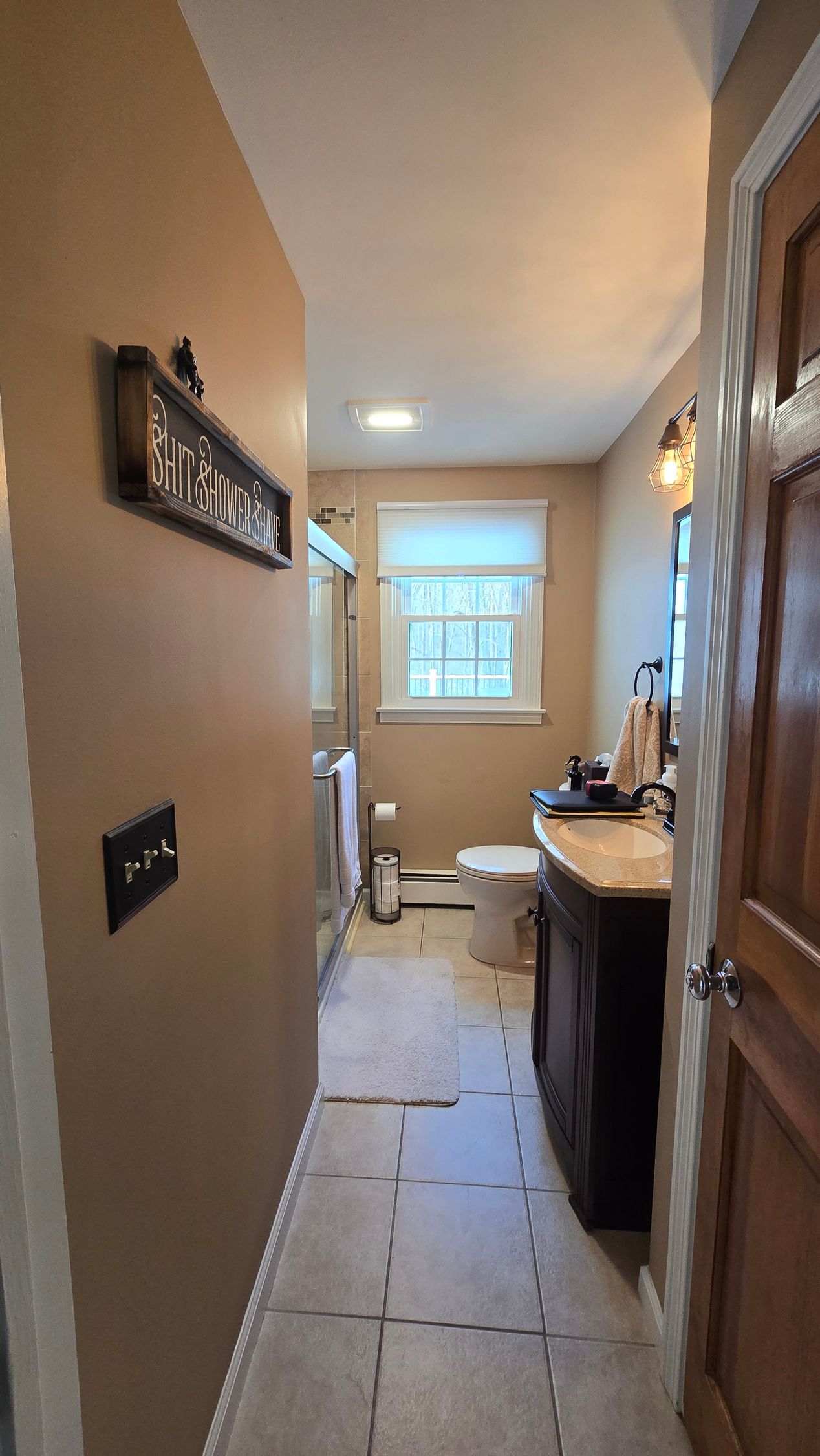Bathroom interior with brown walls, vanity, toilet, and window. Entryway has tile floor in Bristol, CT