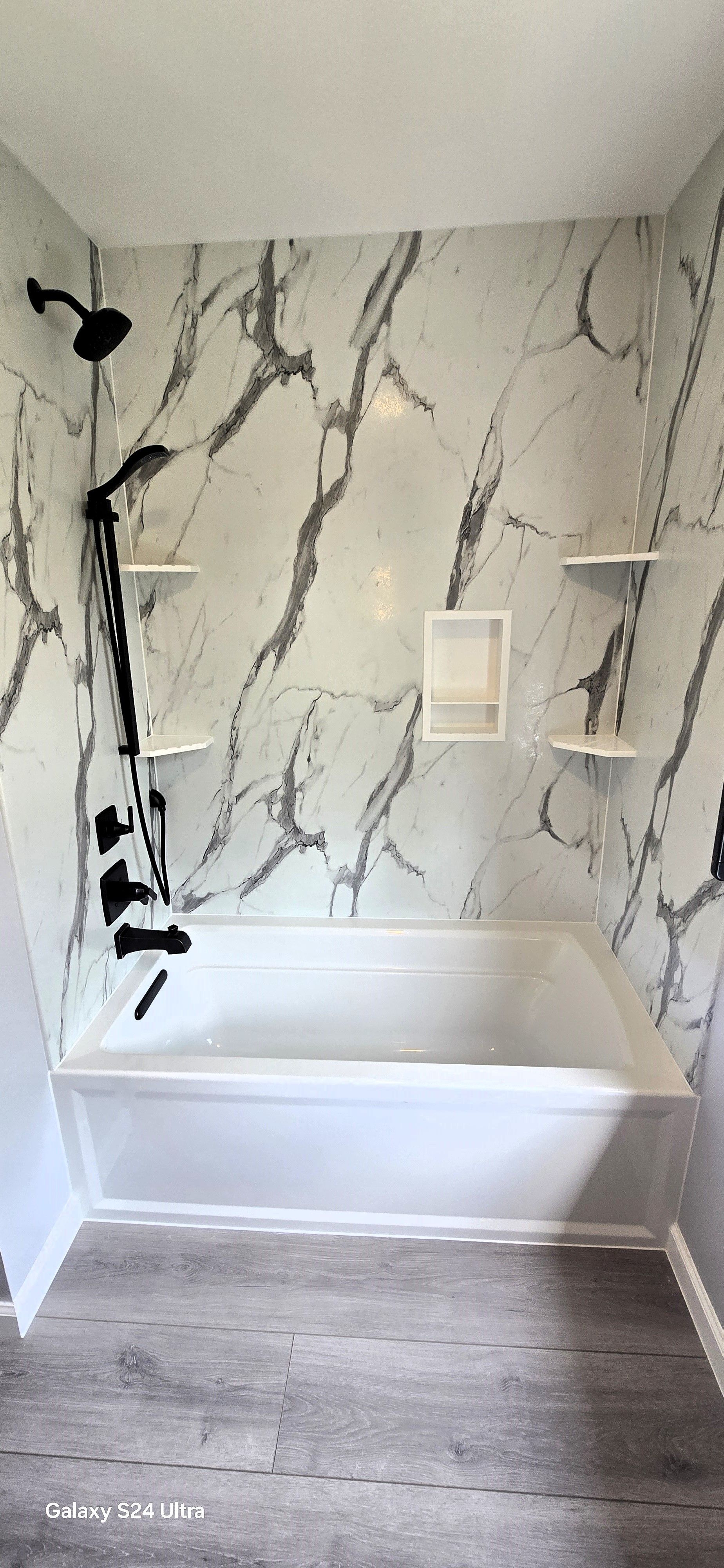A bathroom with a bathtub , shower , and marble wall.