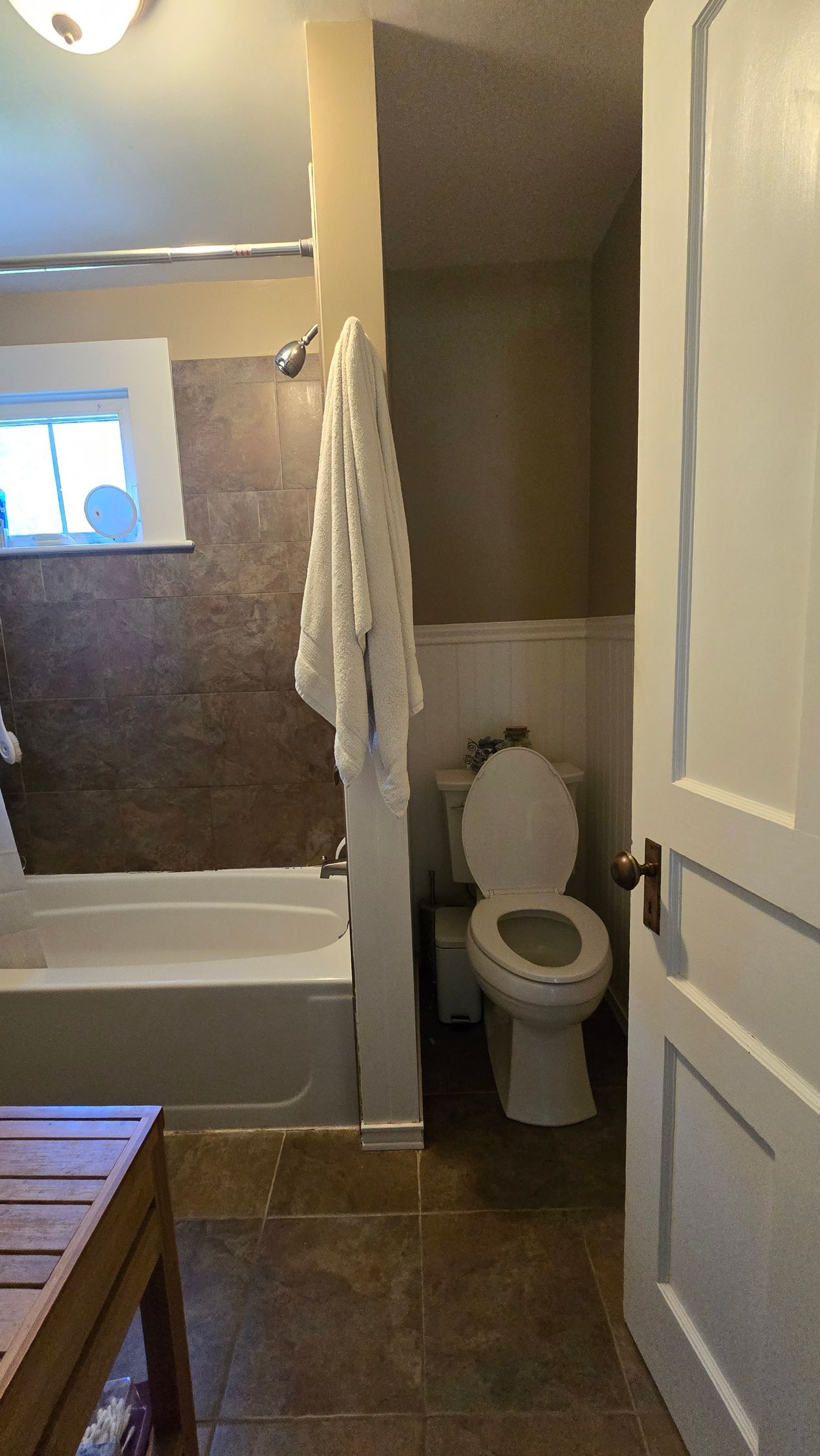 Newington CT bathroom with a tub and toilet. White towel hangs. Brown tile and walls.