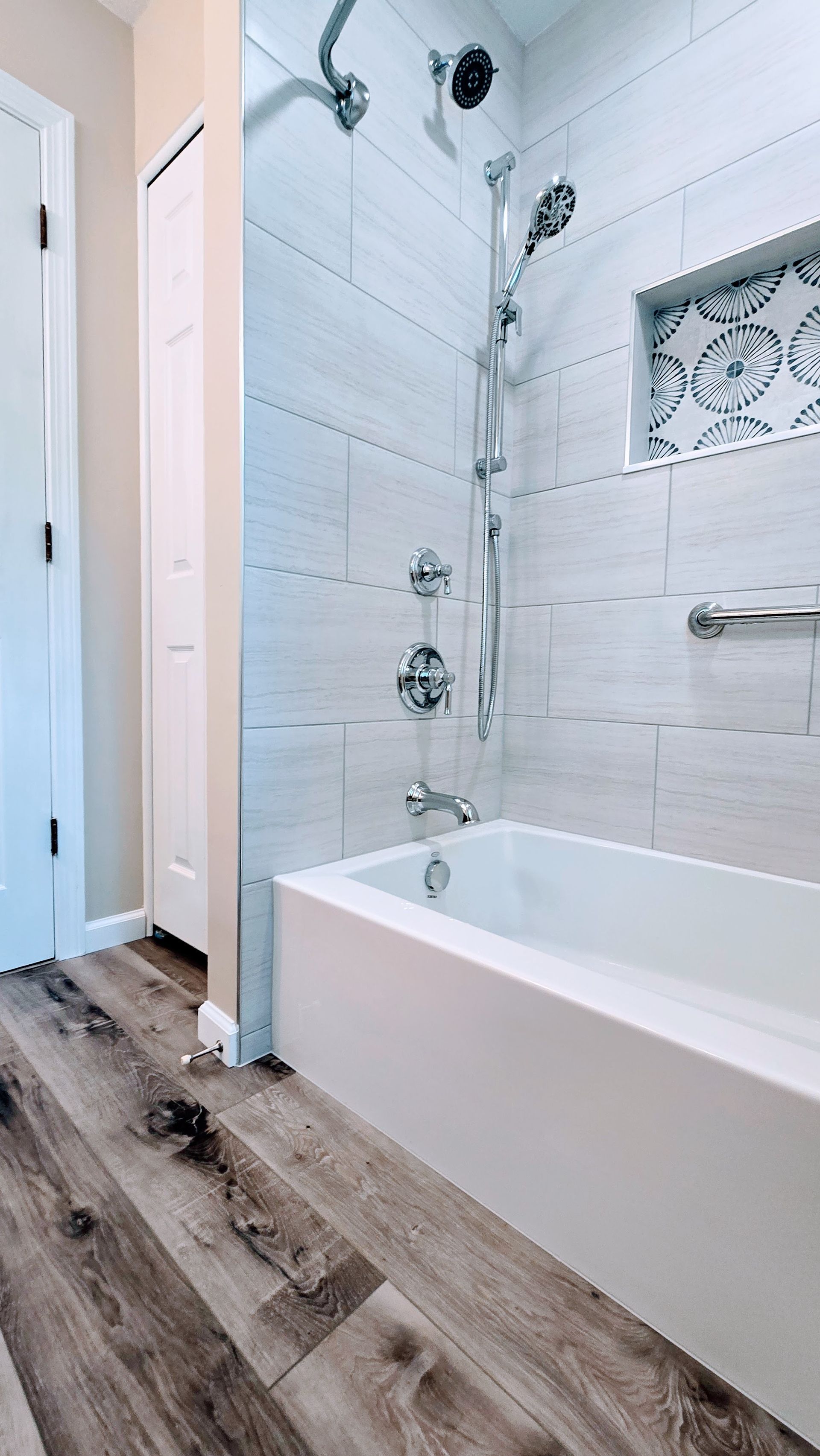 Bathroom with white tub, tiled shower, and wood-look flooring.