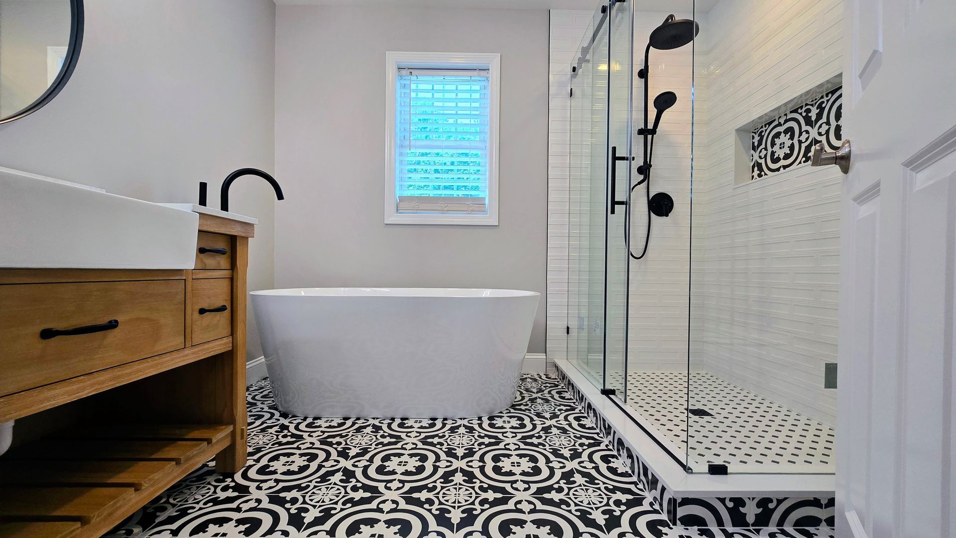 Bathroom iwith patterned floor, white tub, glass shower, and wooden vanity.