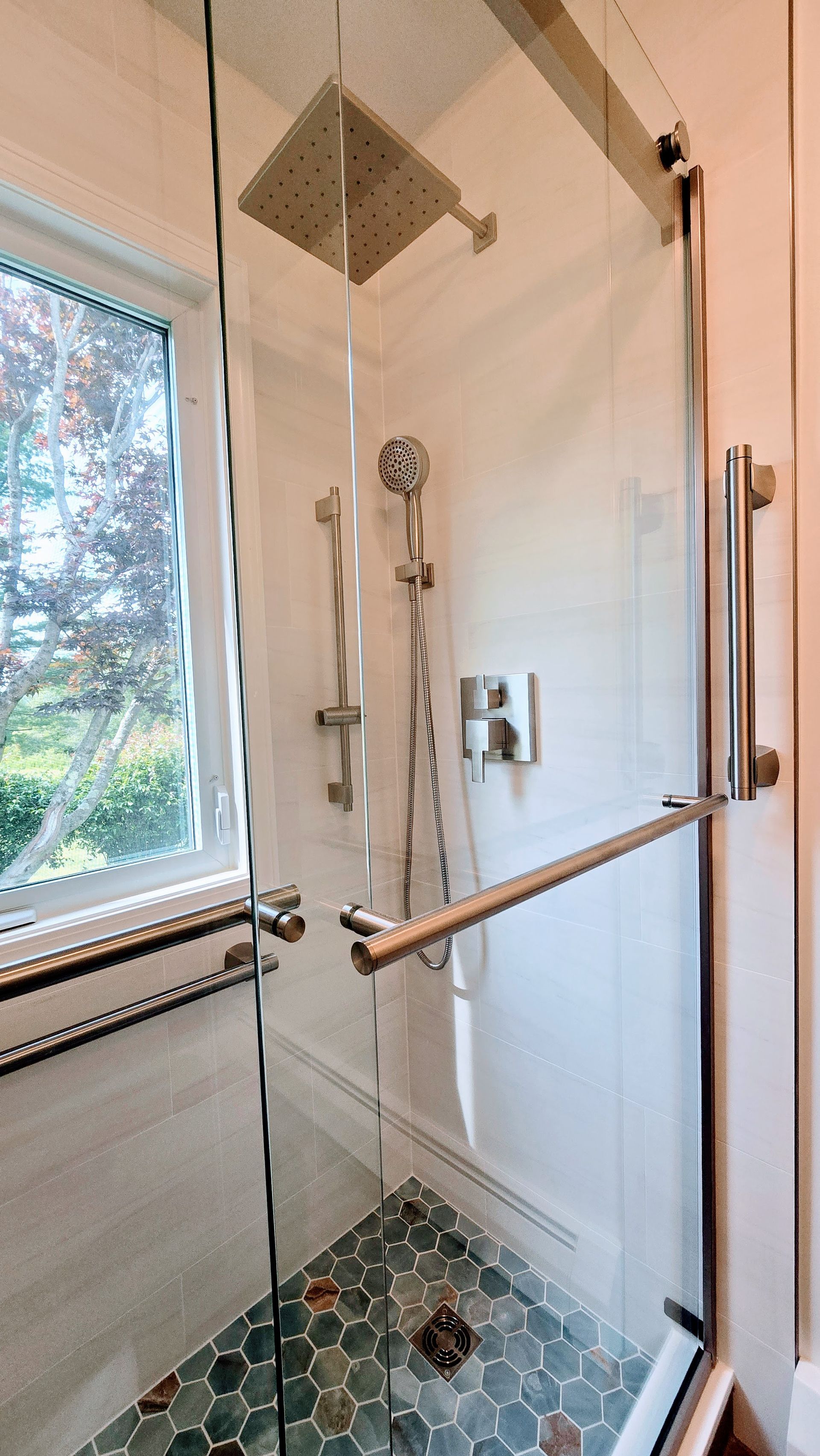 Showerhead and valve on a white-tiled wall. A handheld showerhead hangs, and a temperature/flow control lever is on the right.