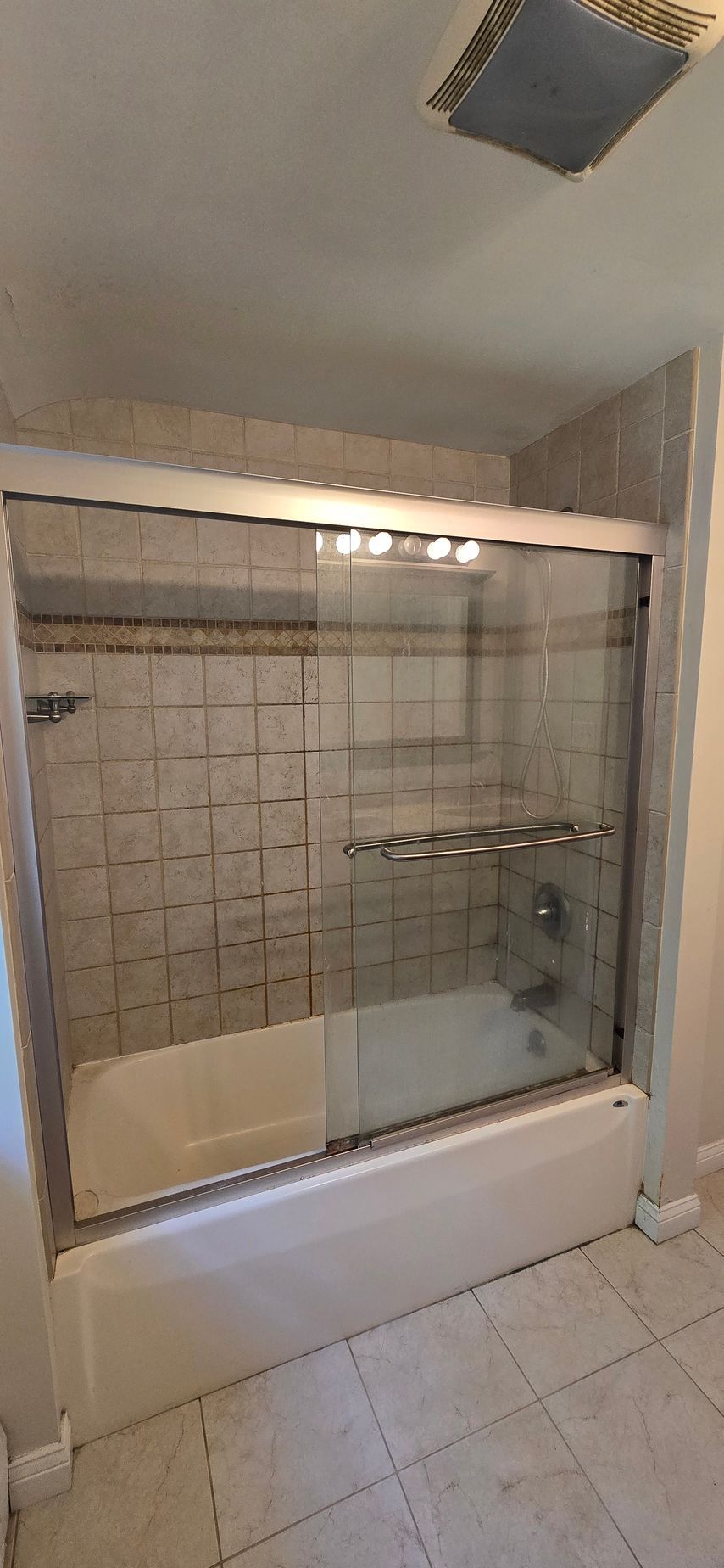 Bathroom with a tub, shower doors, and tile walls. White tub and a tiled floor.