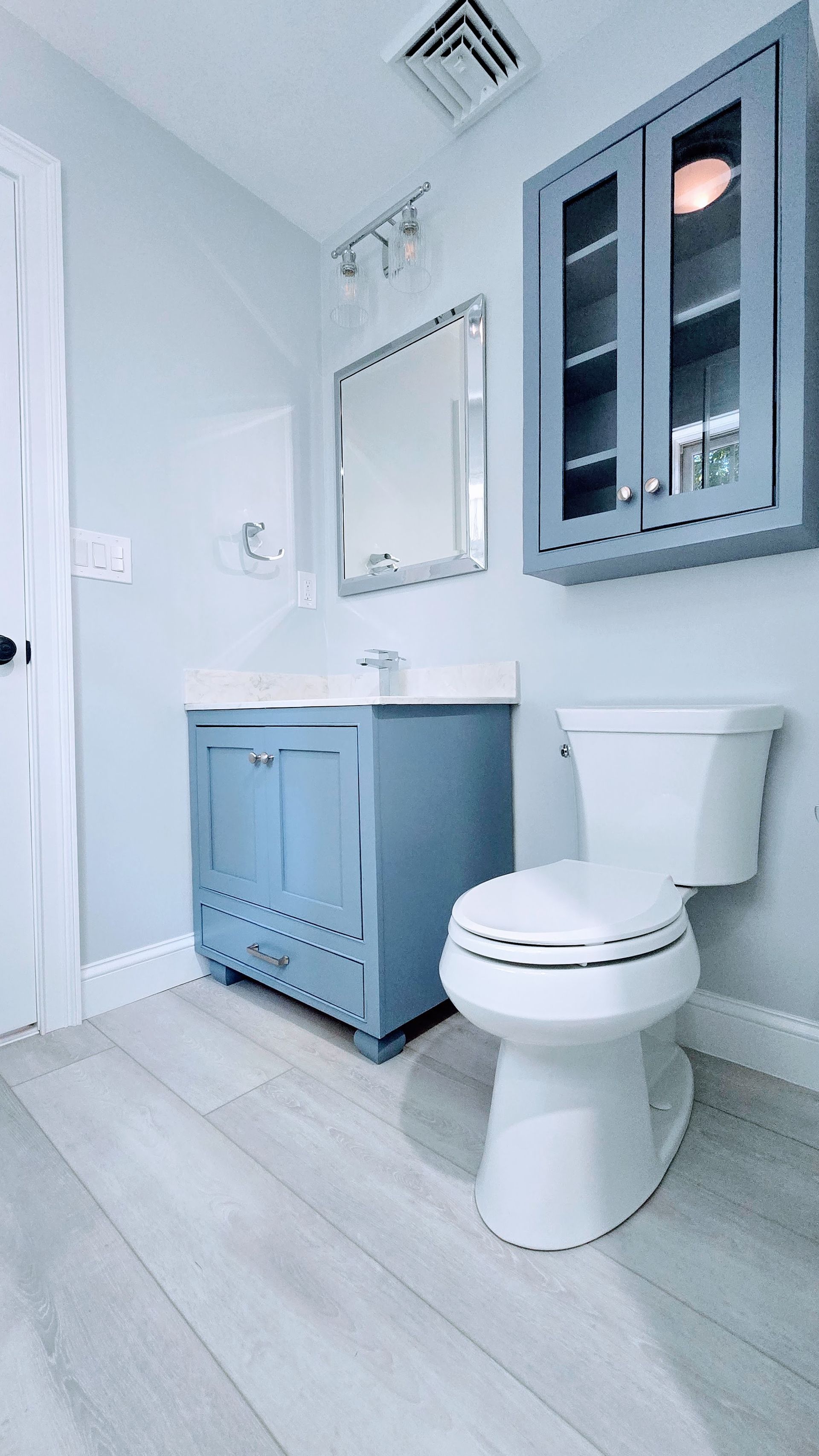 A bathroom with a toilet , sink , mirror and cabinets.