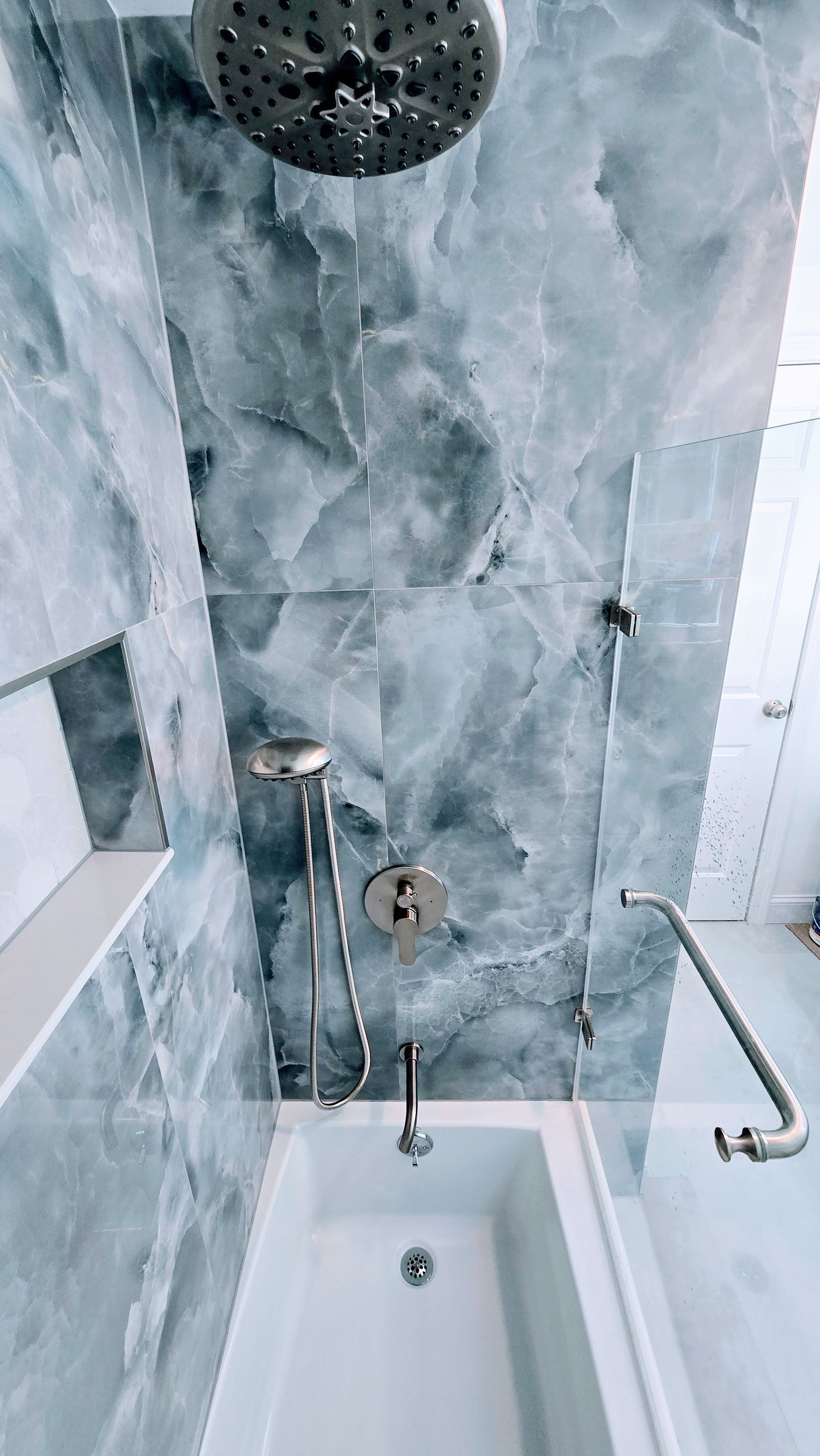 Bathroom with a white West Simsbury bathtub and West Simsbury shower with marbled gray tiles and silver fixtures.