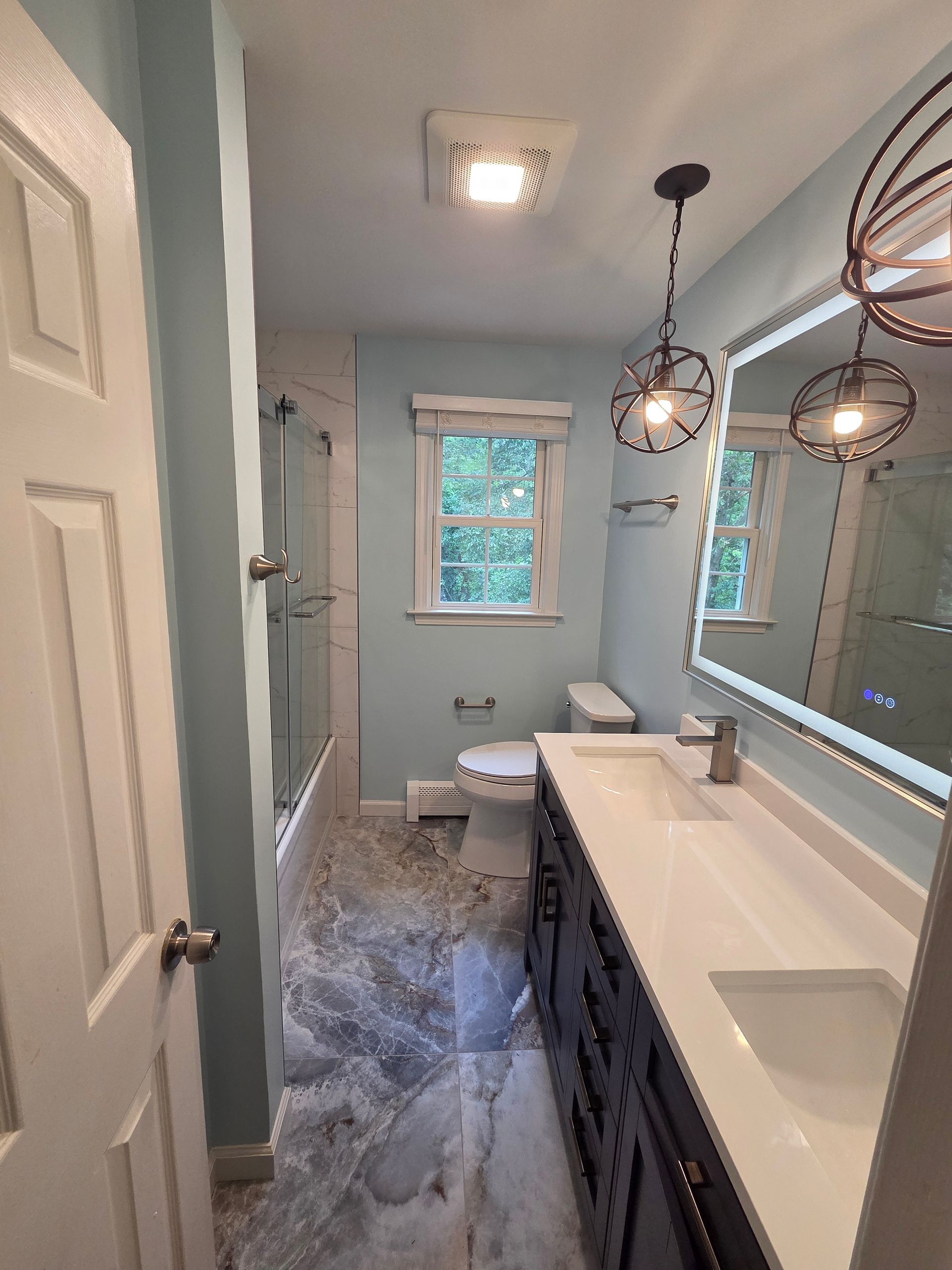 Bathroom with blue walls, gray and white tile floor, dark vanity, and decorative lights.