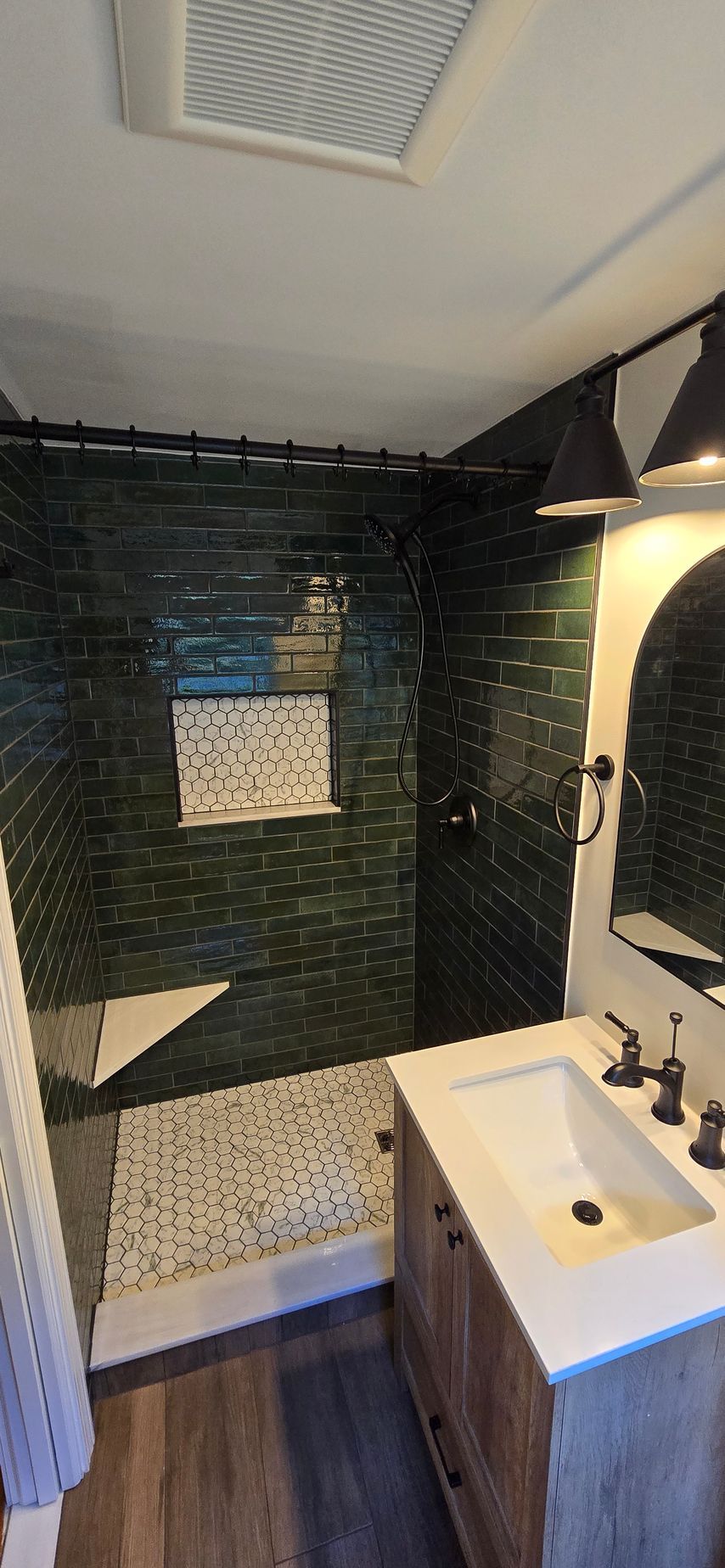 Showerhead and valve on a white-tiled wall. A handheld showerhead hangs, and a temperature/flow control lever is on the right.