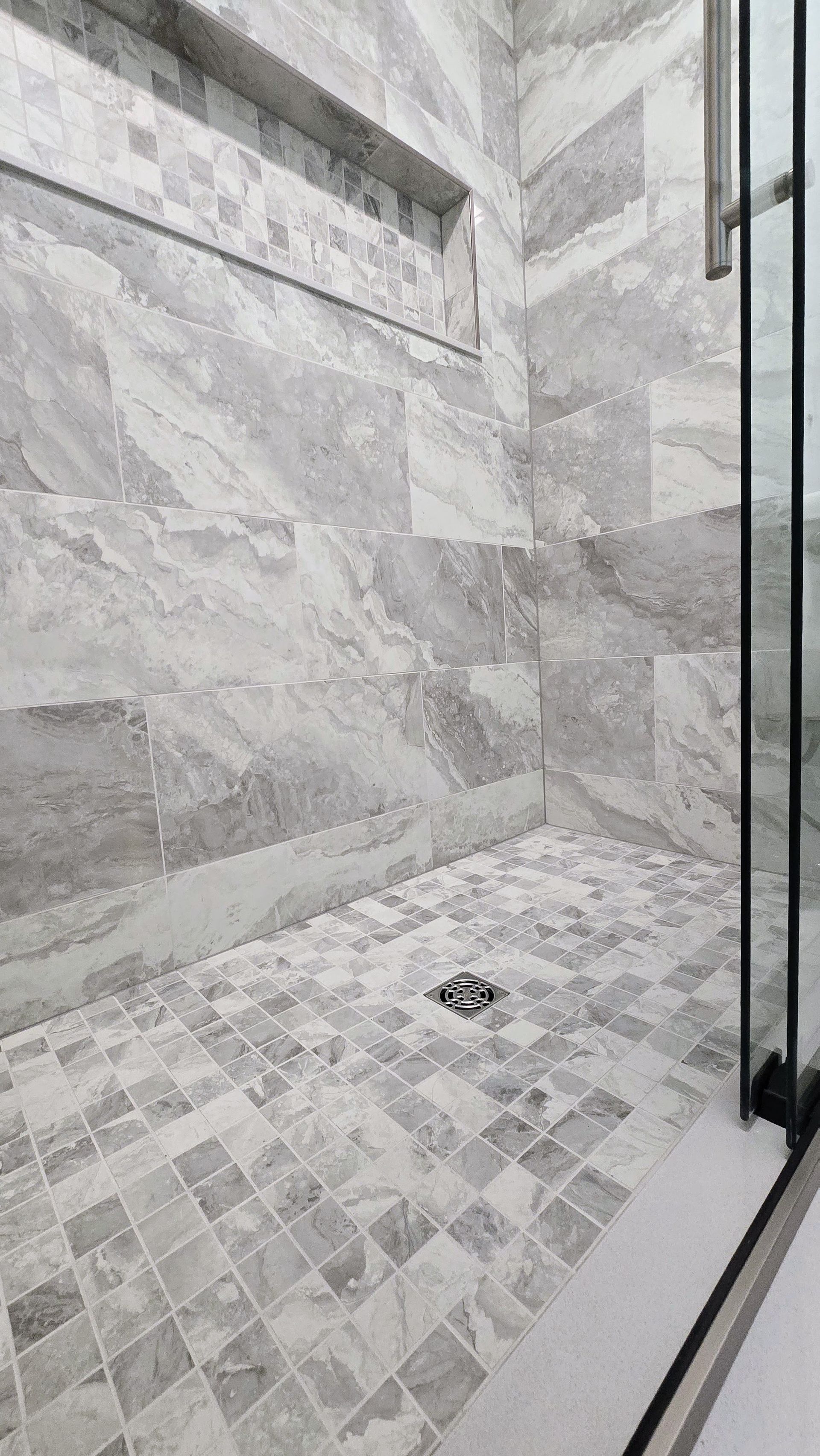 Gray and white marble tiled shower with glass door and recessed shelf in Plainville, CT