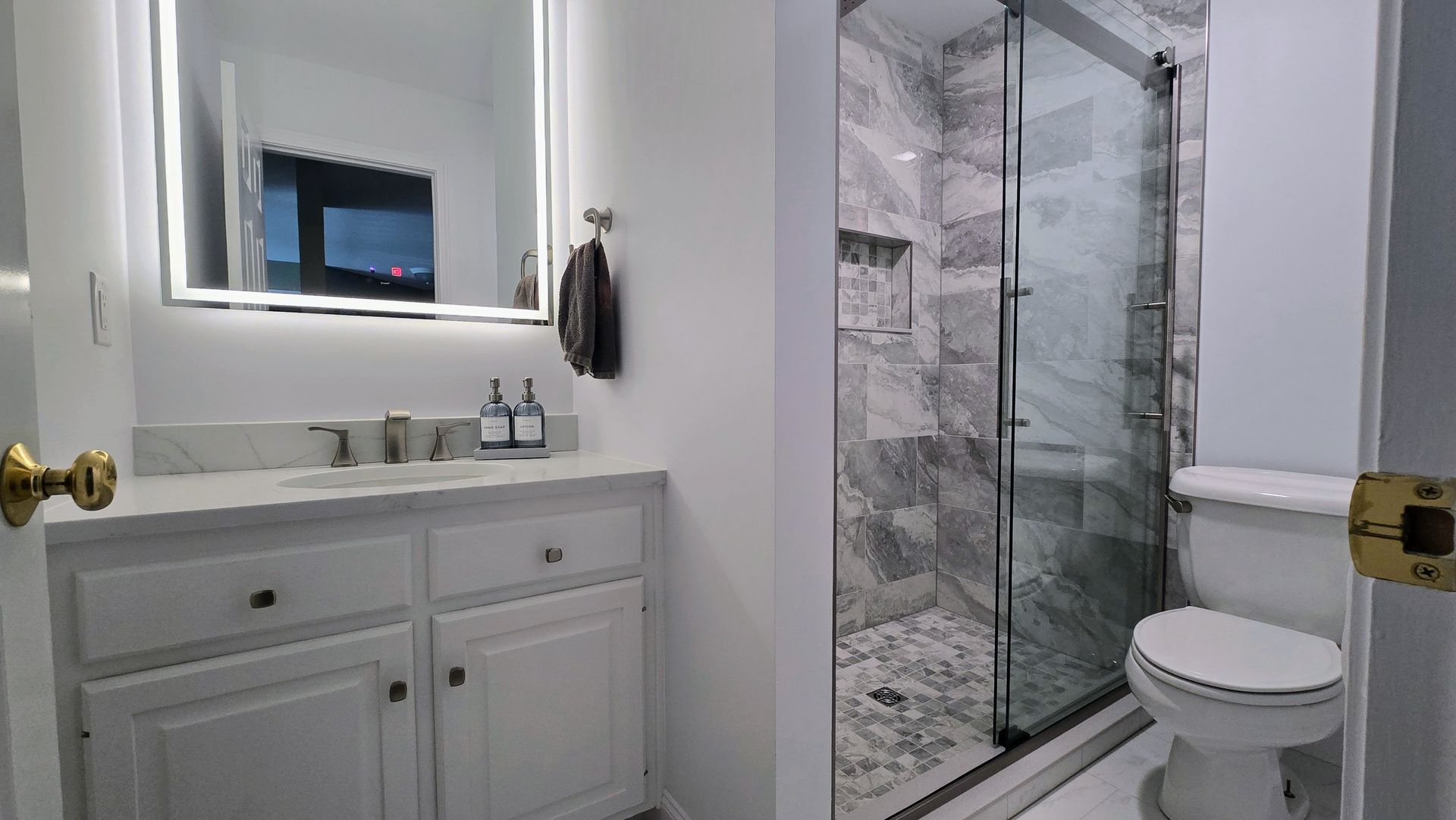Bathroom with marble walk-in shower and vanity, lit mirror, white cabinets, and toilet in Plainville, CT