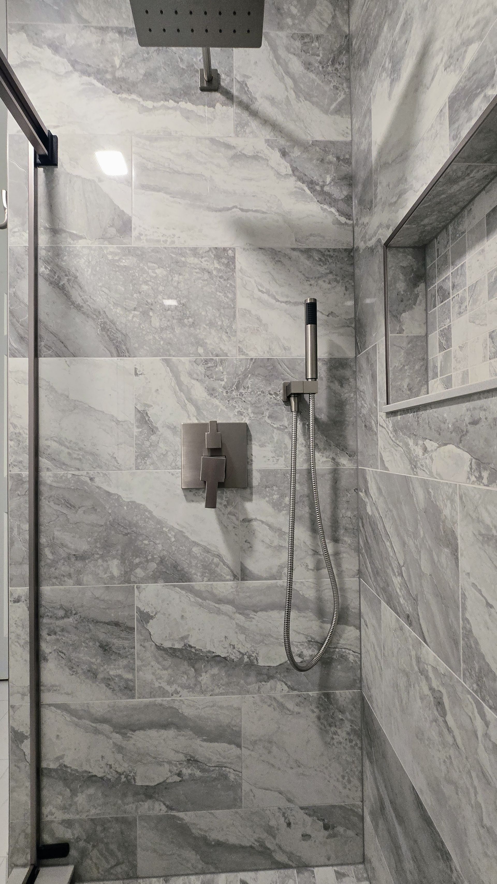 Gray marble tiled shower with overhead showerhead, handheld shower, and recessed shelf in Plainville, CT