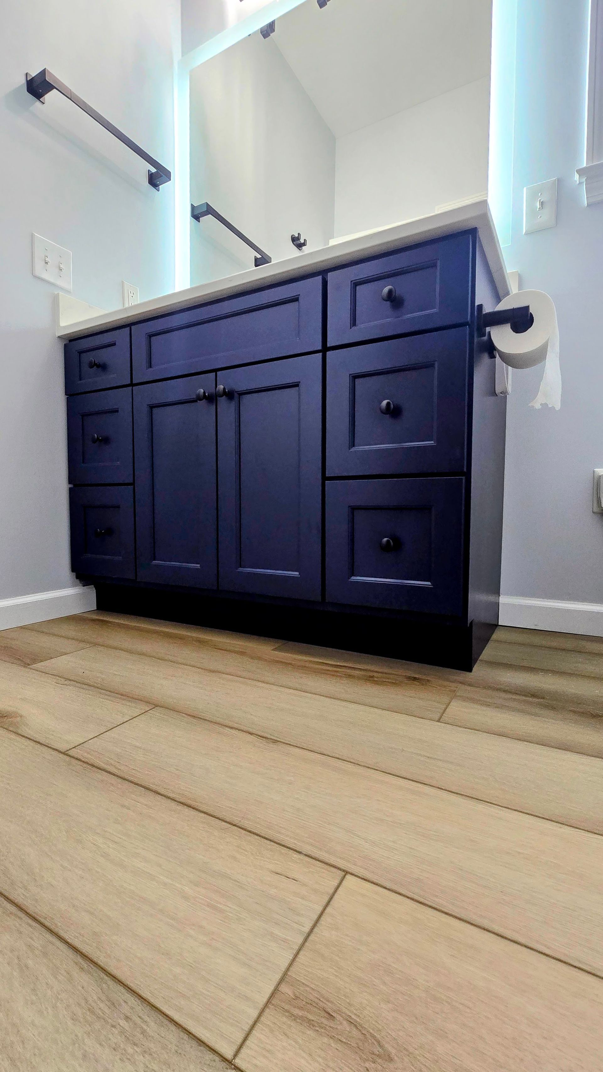 Dark blue bathroom vanity with drawers and cabinets, white countertop. Light wood-look flooring.