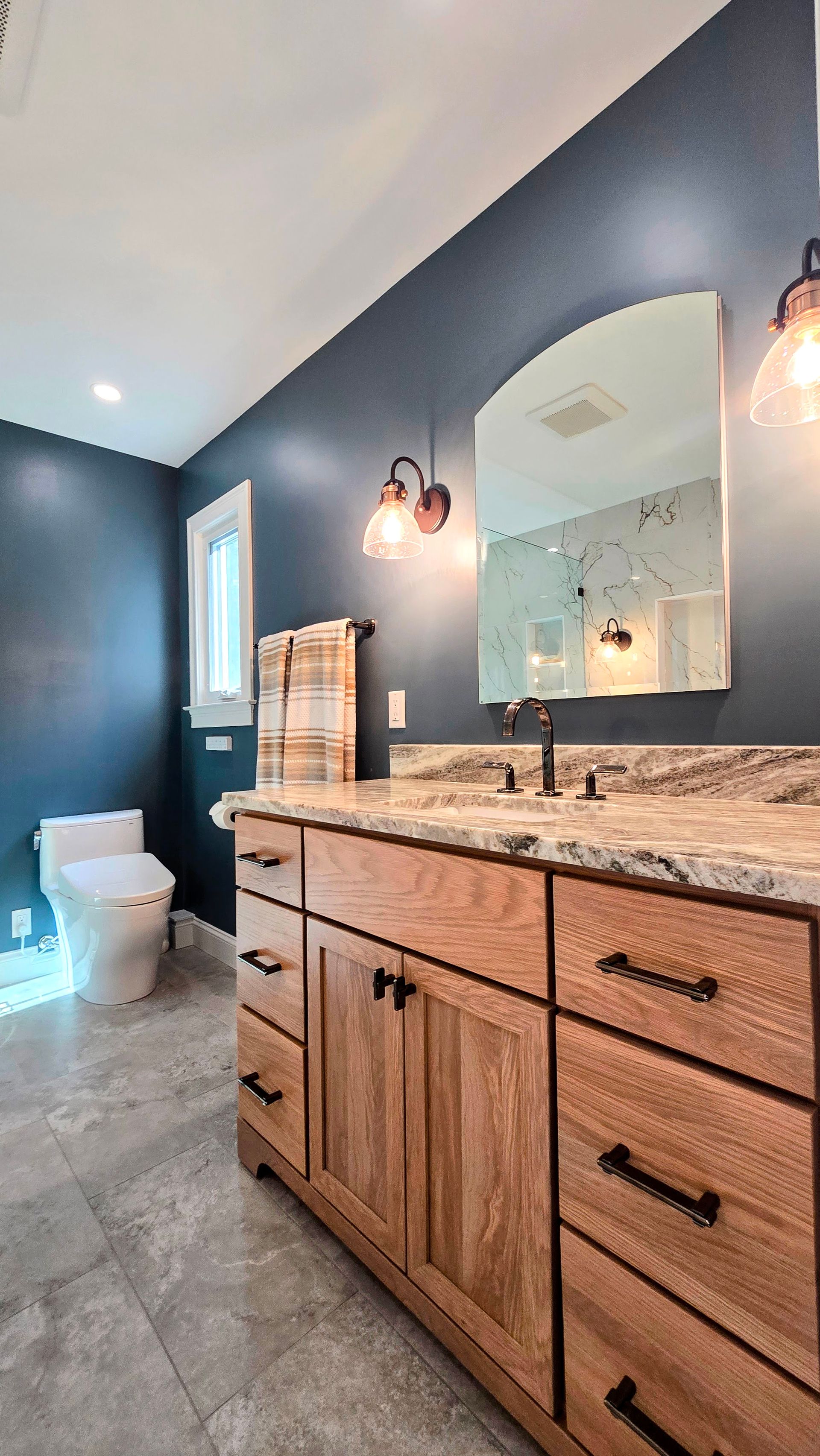 Finished Bathroom renovation in Avon, CT with wooden vanity, navy blue walls, and gray tile floor.