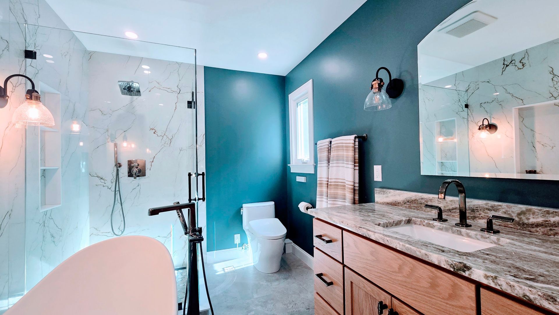 Modern bathroom in Avon, CT with marble shower, teal walls, wood vanity, and a tub.