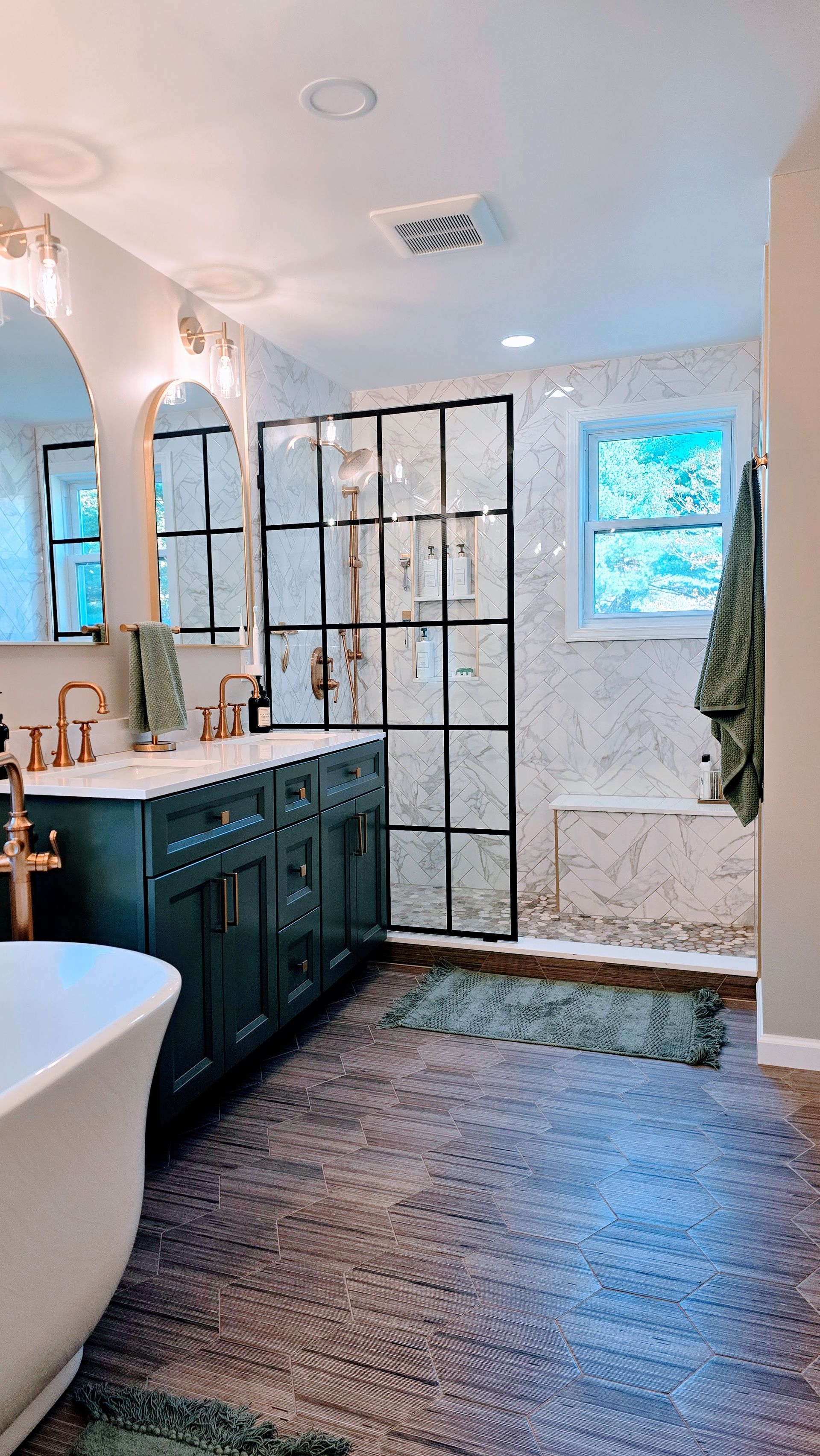 Modern bathroom renovation in Wolcott, CT with dark green vanity, glass shower enclosure, and gray patterned rug.