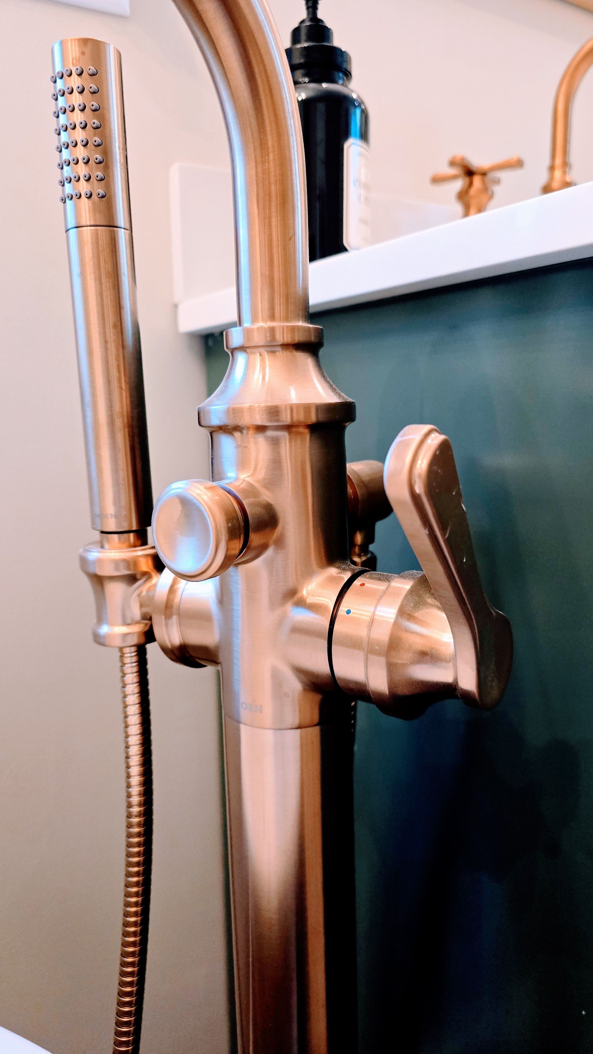 Bronze floor-mounted faucet with handheld shower head; lever and knob controls.