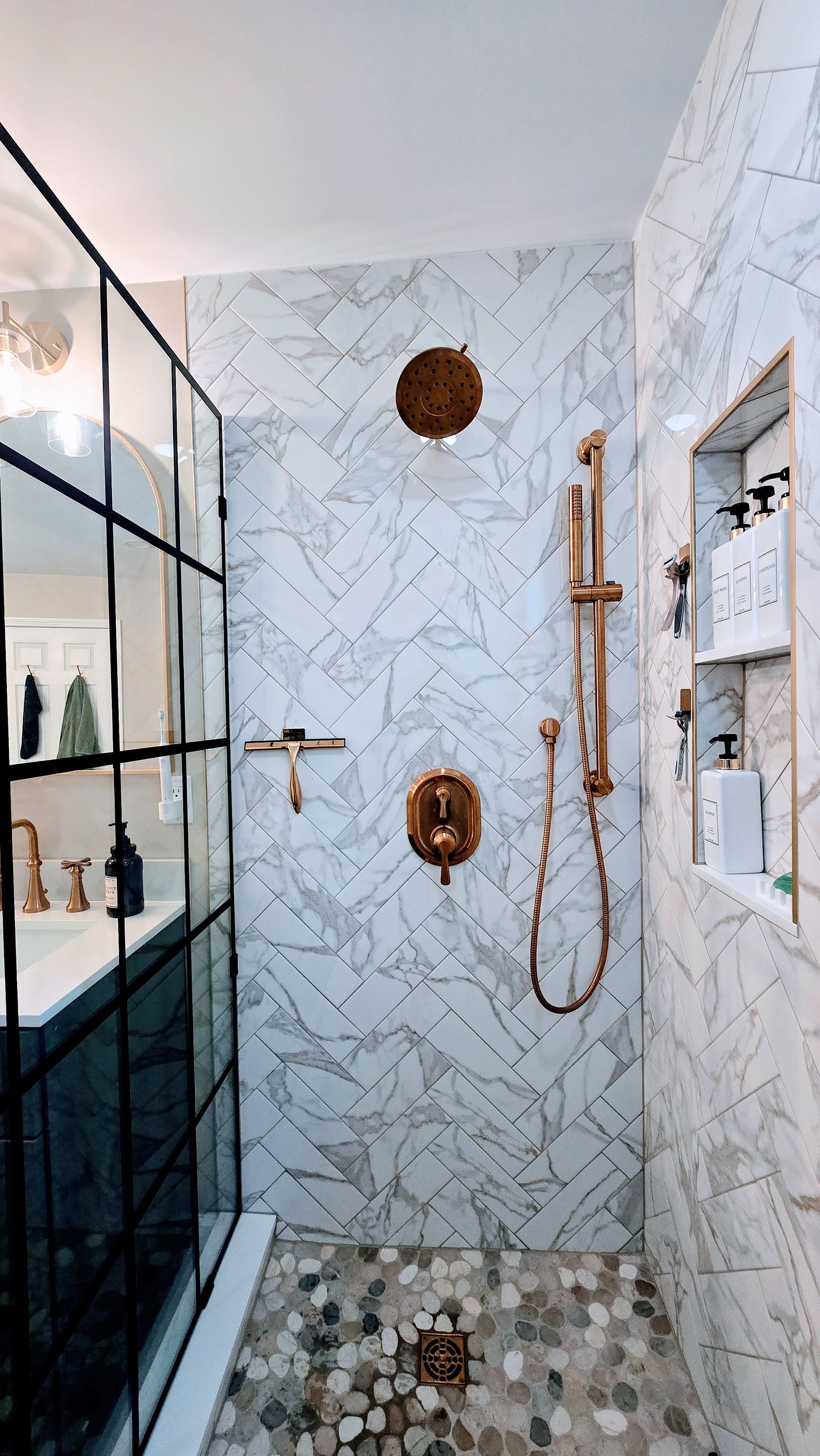 Modern shower remodel in Wolcott, CT with white herringbone tile, gold fixtures, and a black-framed glass door.