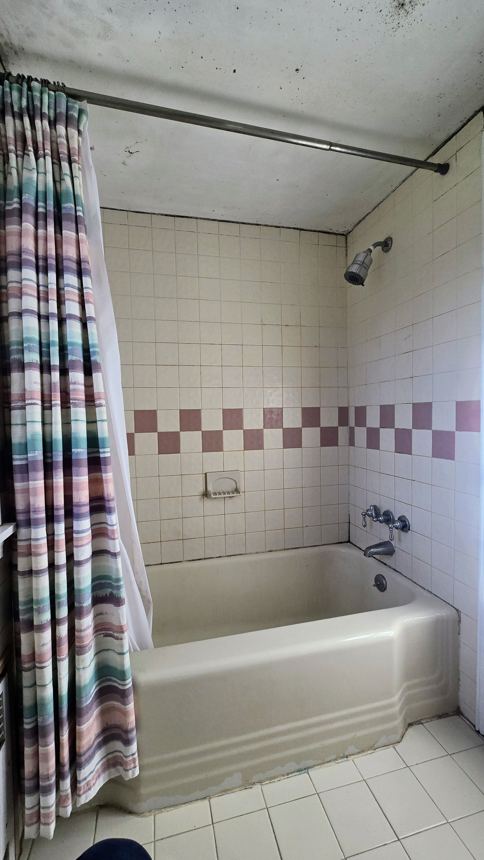 A beige Southington CT bathtub with a pink and white tiled wall and a colorful shower curtain.