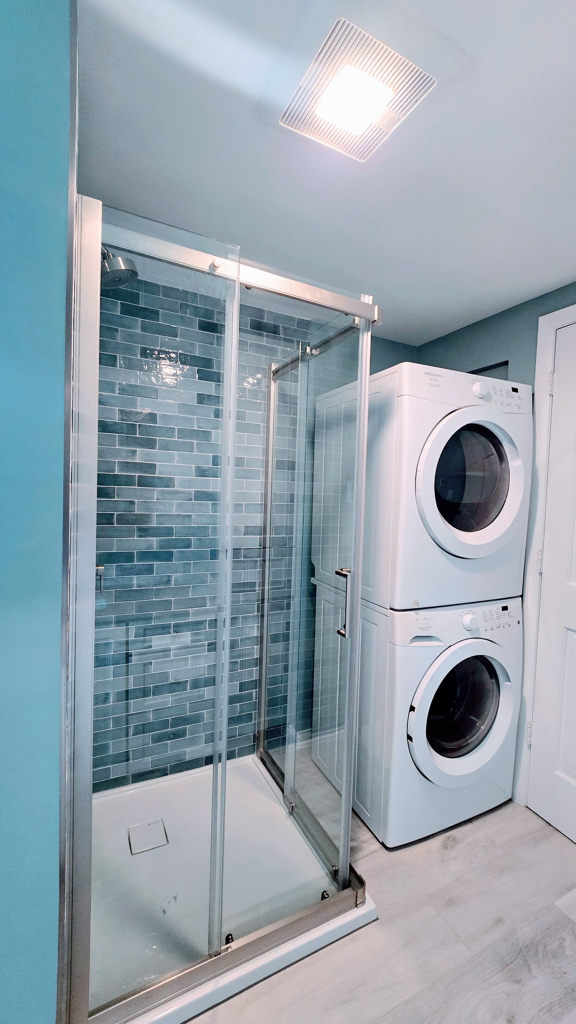 Small bathroom remodel in Ashford, CT with a shower and stacked white washer/dryer against blue walls.