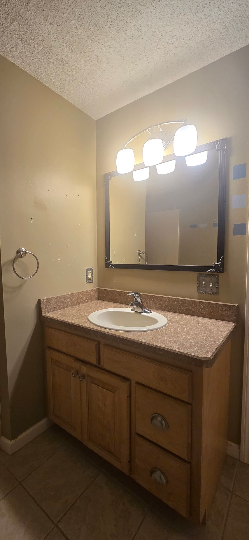 Bathroom vanity with mirror, light fixtures, and sink. Beige walls, light brown cabinet and countertop.