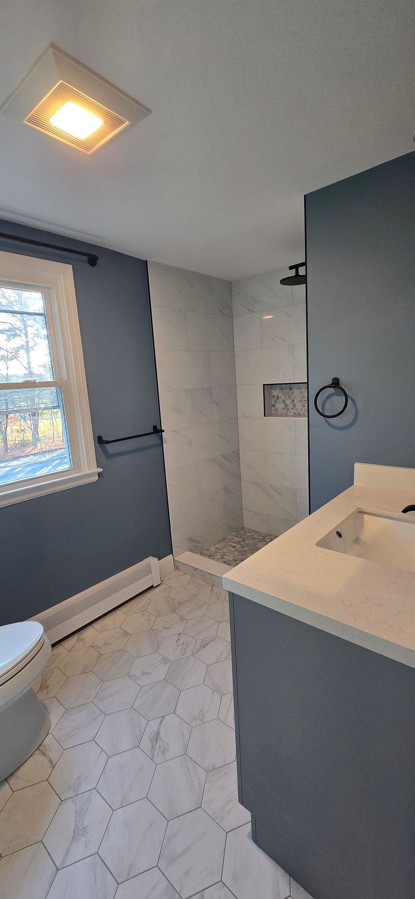 A modern bathroom in Berlin with a blue wall, white marble shower, and gray vanity with white countertop.