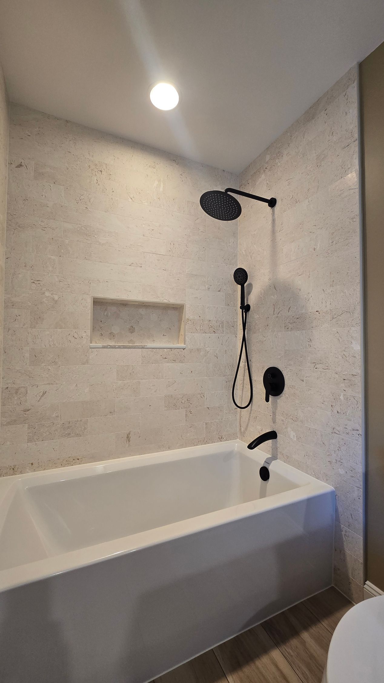 Bristol bathroom with white tub, stone tile walls, black shower fixtures, and a recessed shelf.