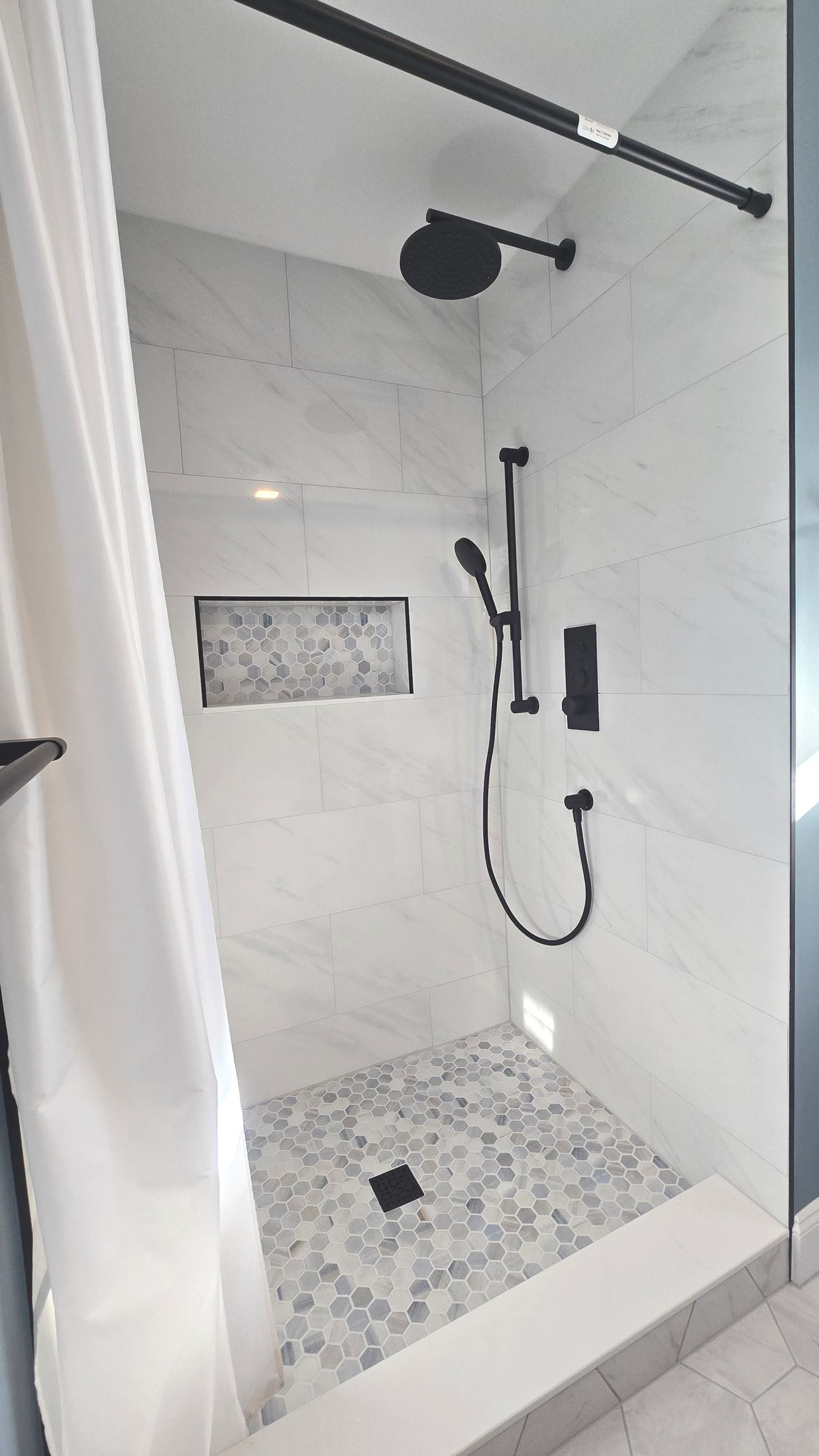 Luxurious bathroom remodel in Wolcott, CT with dark green vanity, white tub, gold fixtures, and arched mirror.