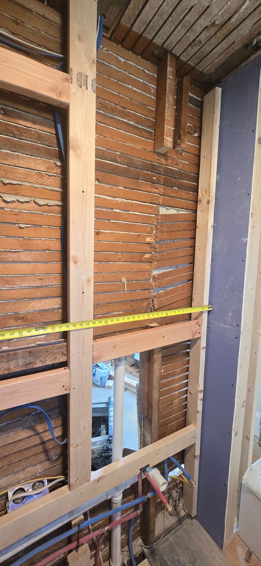 Construction of a Newington CT wall frame with exposed lathe and plaster. A measuring tape is stretched across the frame. Done by First Choice.