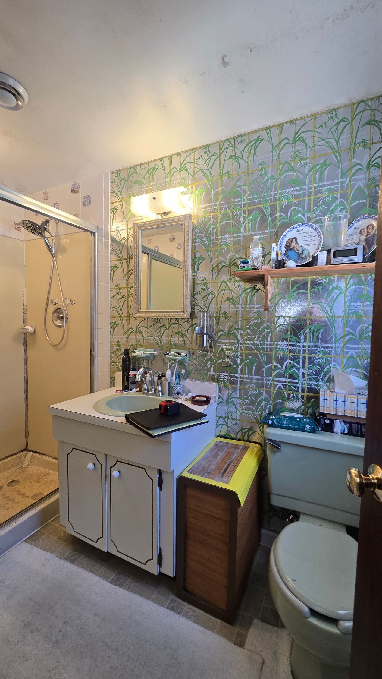 Small bathroom with white vanity, mirror, toilet, and tiled shower beside green patterned wall.