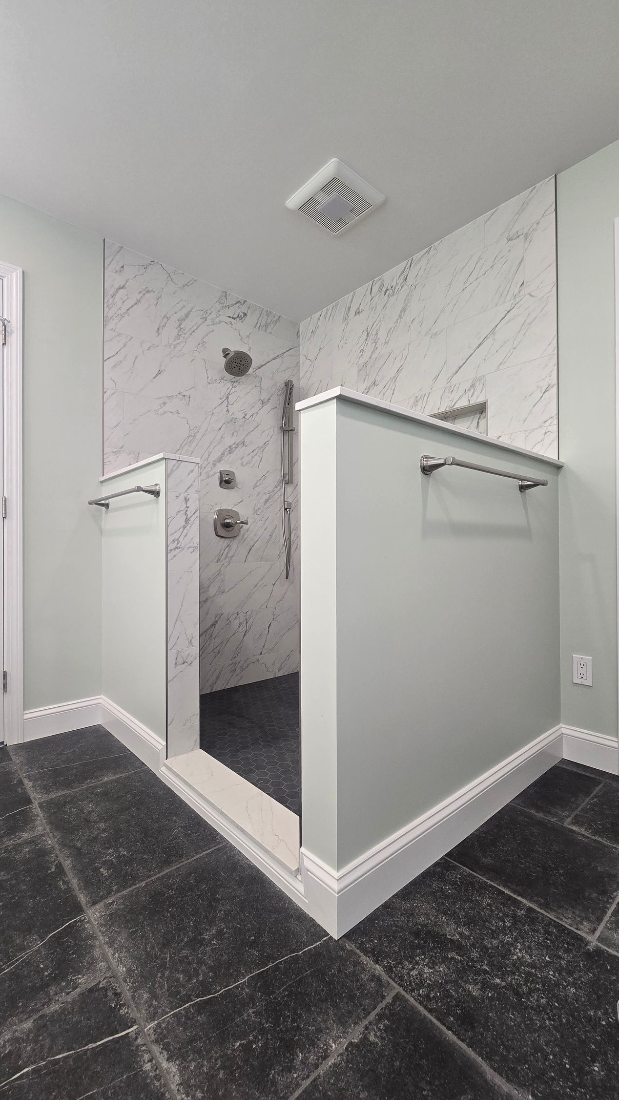 Bathroom with walk-in shower in Glasonbury, CT, featuring marble walls, black floor tiles, and mint green half walls.