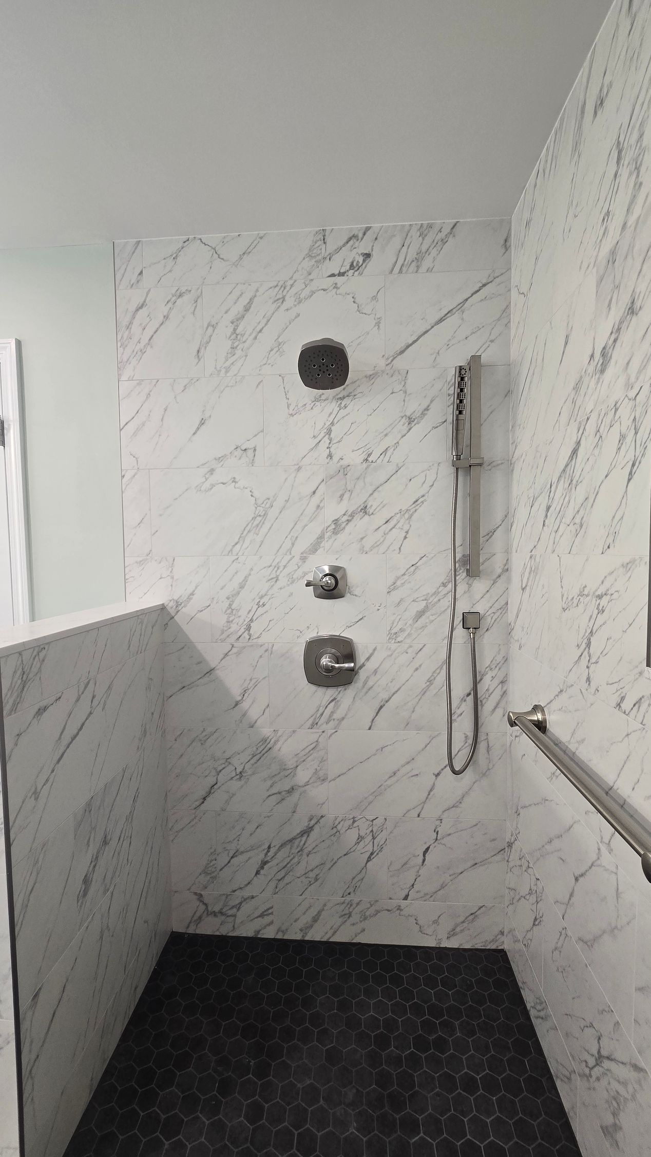 Luxury white marble-tiled shower in Glastonbury, CT with black tiled floor and silver shower fixtures.