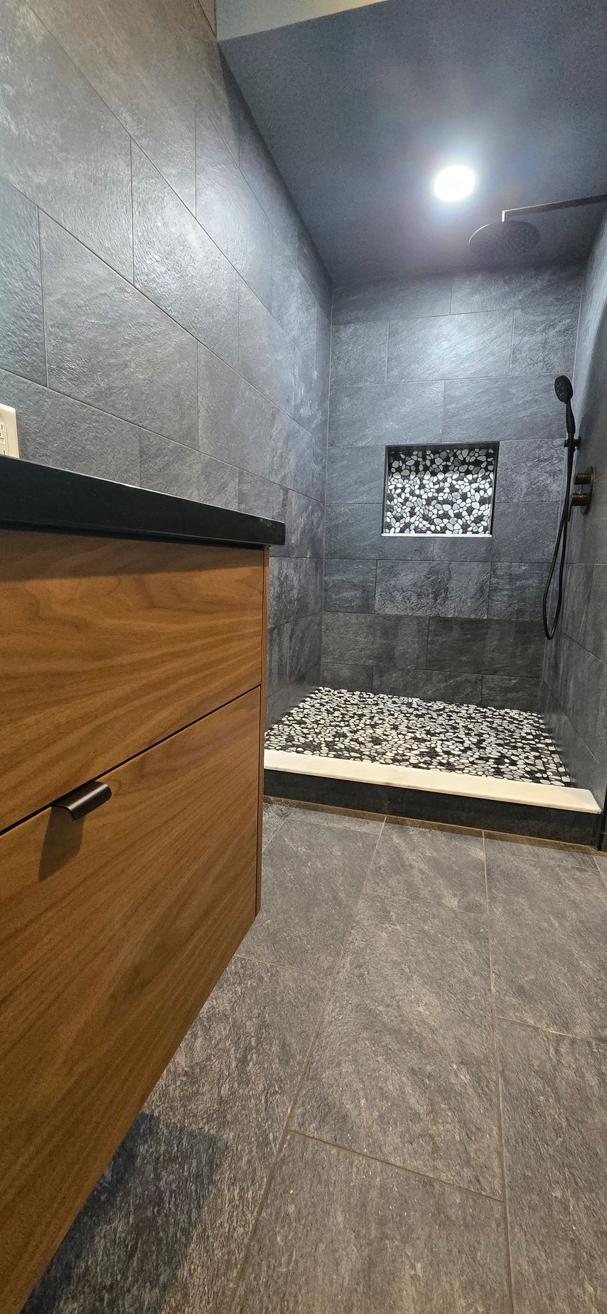 Bristol bathroom with white tub, stone tile walls, black shower fixtures, and a recessed shelf.