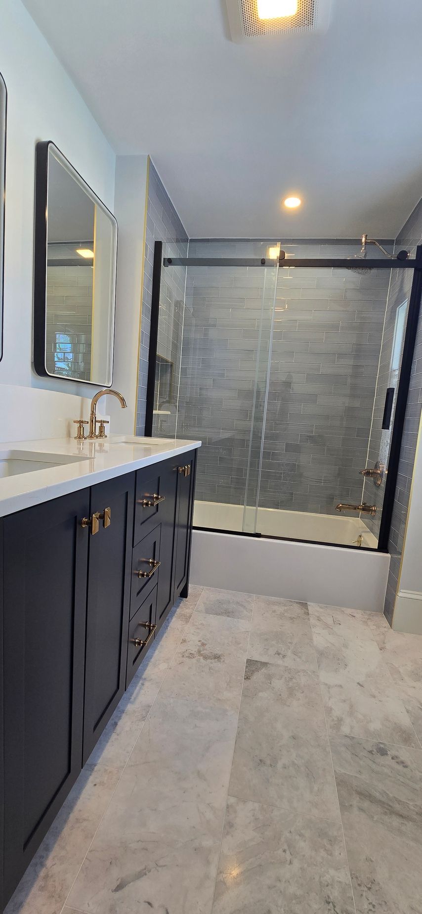 Newington CT bathroom with navy vanity, marble floor, glass shower, and gray tile. Done by First Choice Bathroom Remodeling.