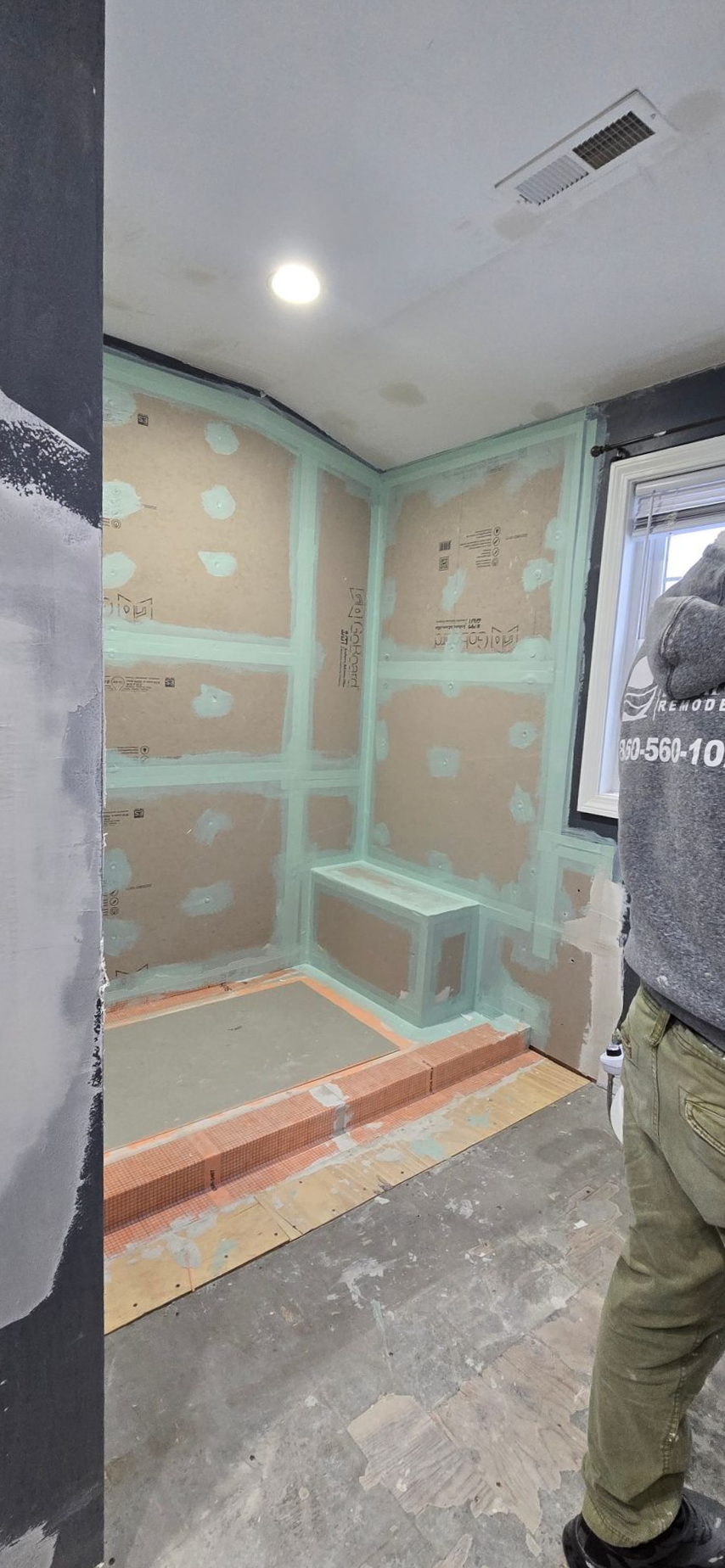 Bathroom under construction with green waterproof drywall. A person stands on the right.