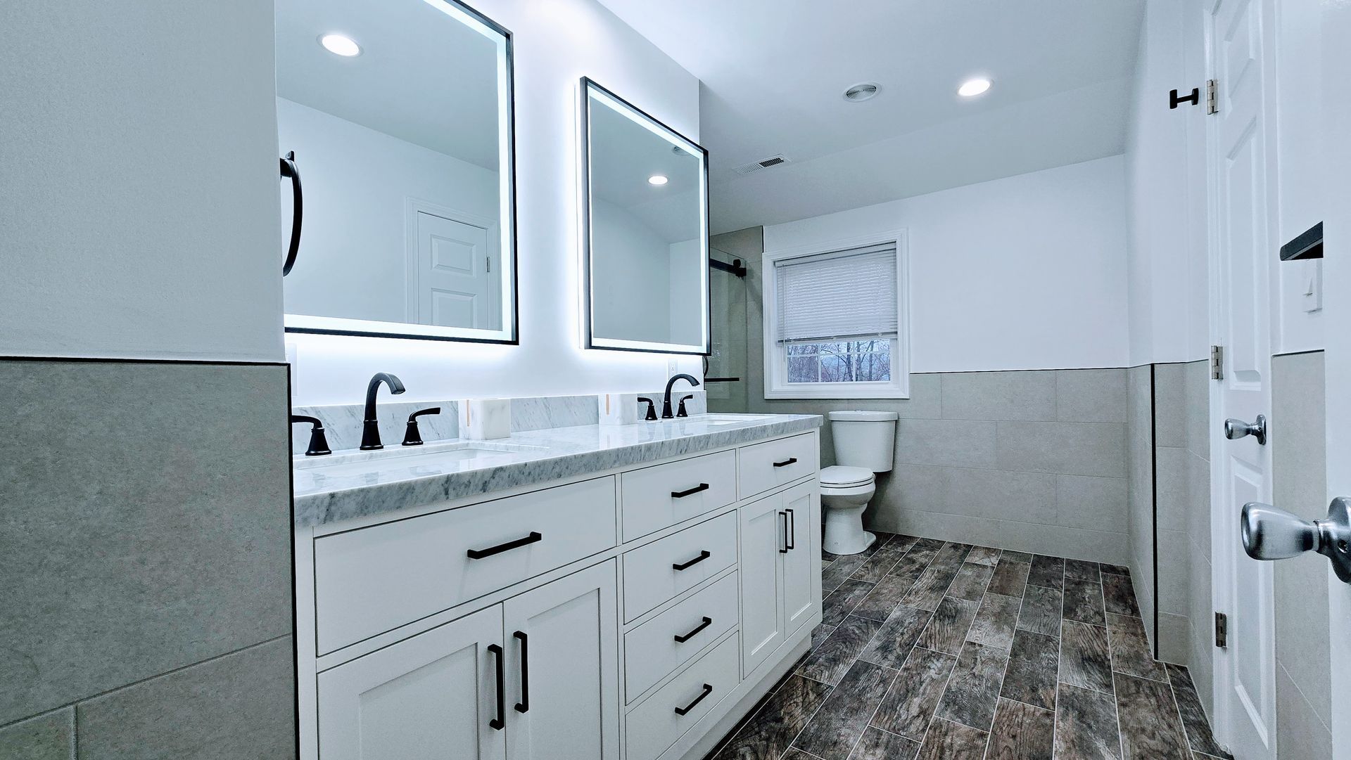 Modern bathroom in Berlin, CT with white vanity, black hardware, framed mirrors, and wood-look tile.