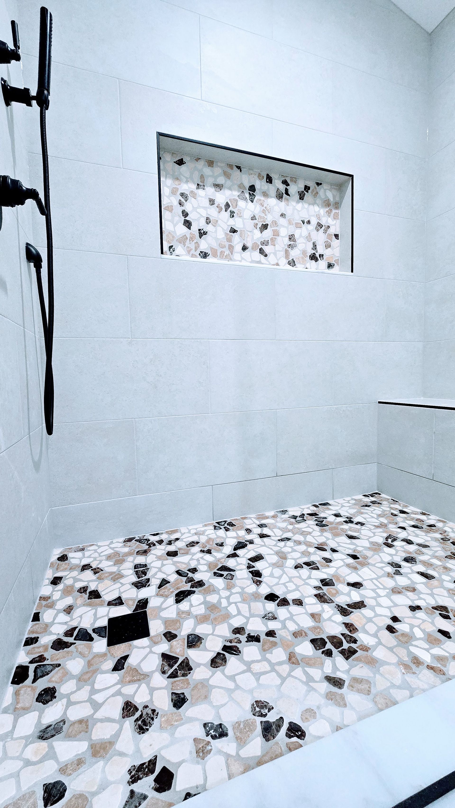 Shower in Berlin, CT with gray, white, and black patterned tile floor and accent wall. Built-in shelf, black shower fixture.