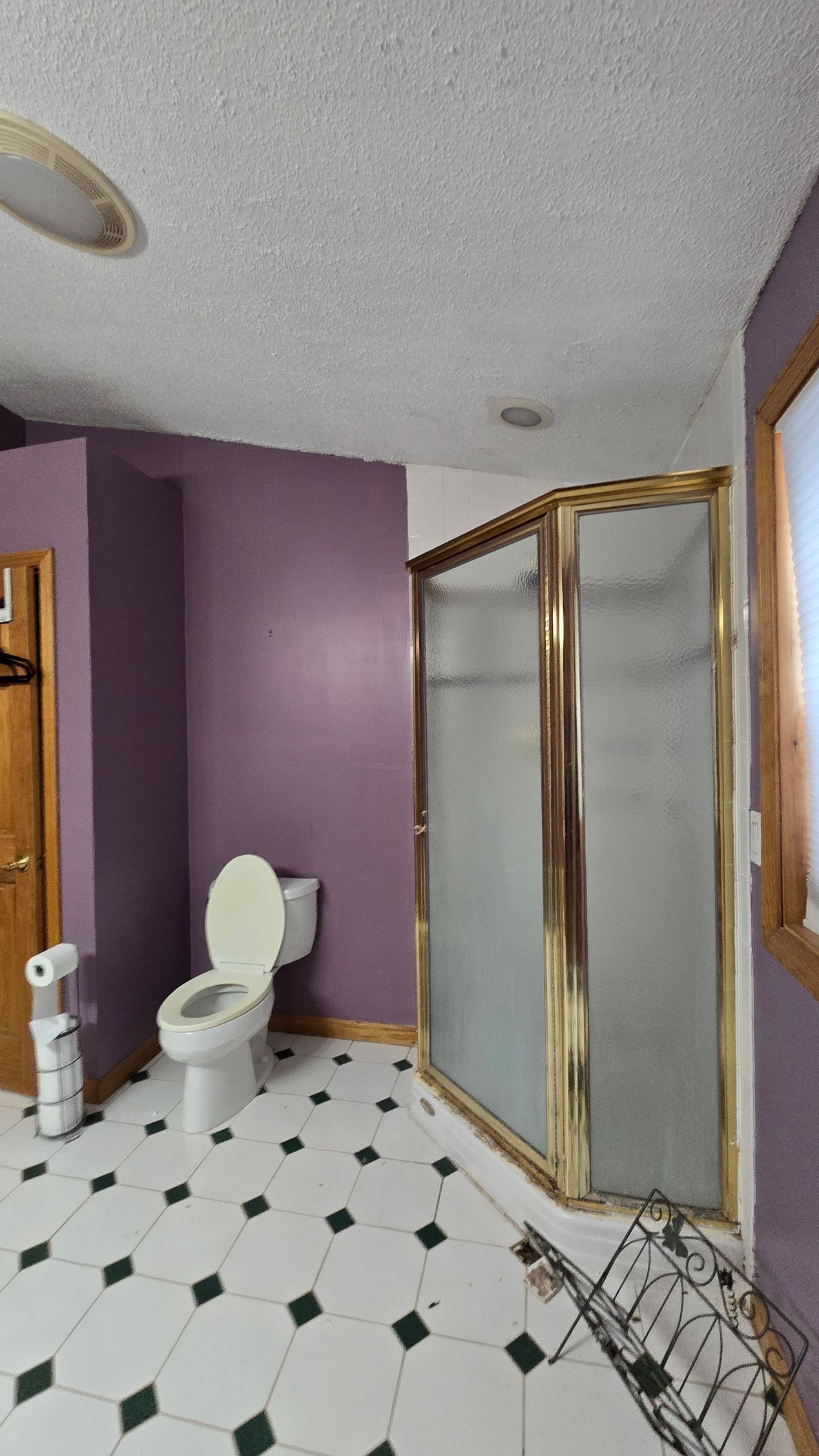 Bathroom with white tile floor, purple wall, toilet, glass shower enclosure, and wooden window frame.