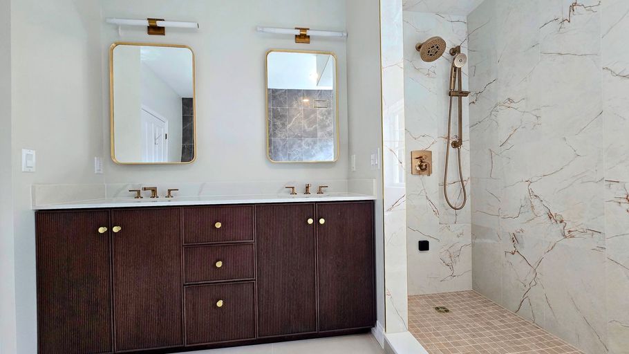 A modern bathroom in Cromwell, CT featuring a dark wood double vanity with gold hardware, two rectangular mirrors, and a marble shower.