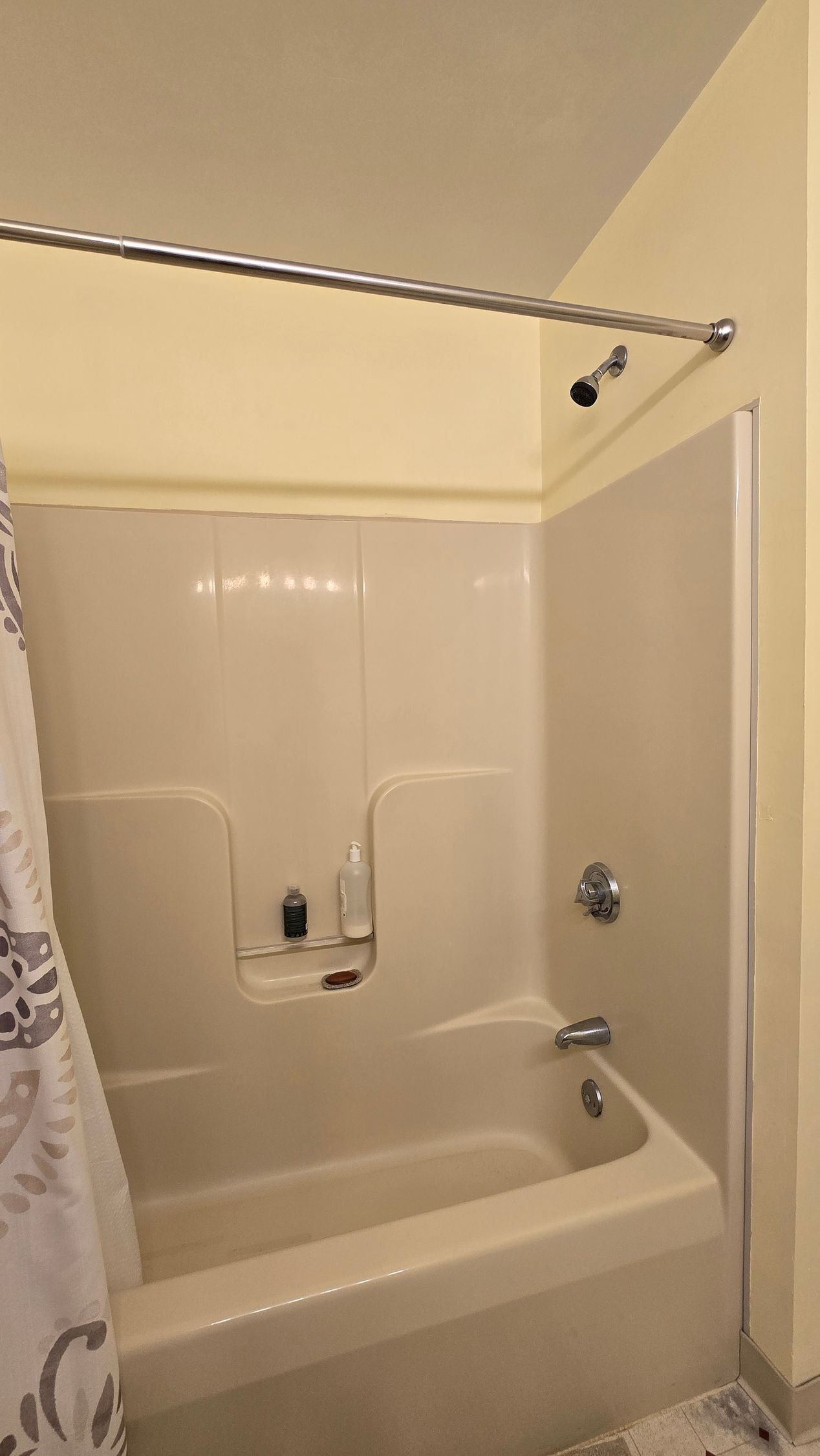 Accessible bathtub and shower with grab bars, fold-down seat, and handheld showerhead in a beige bathroom