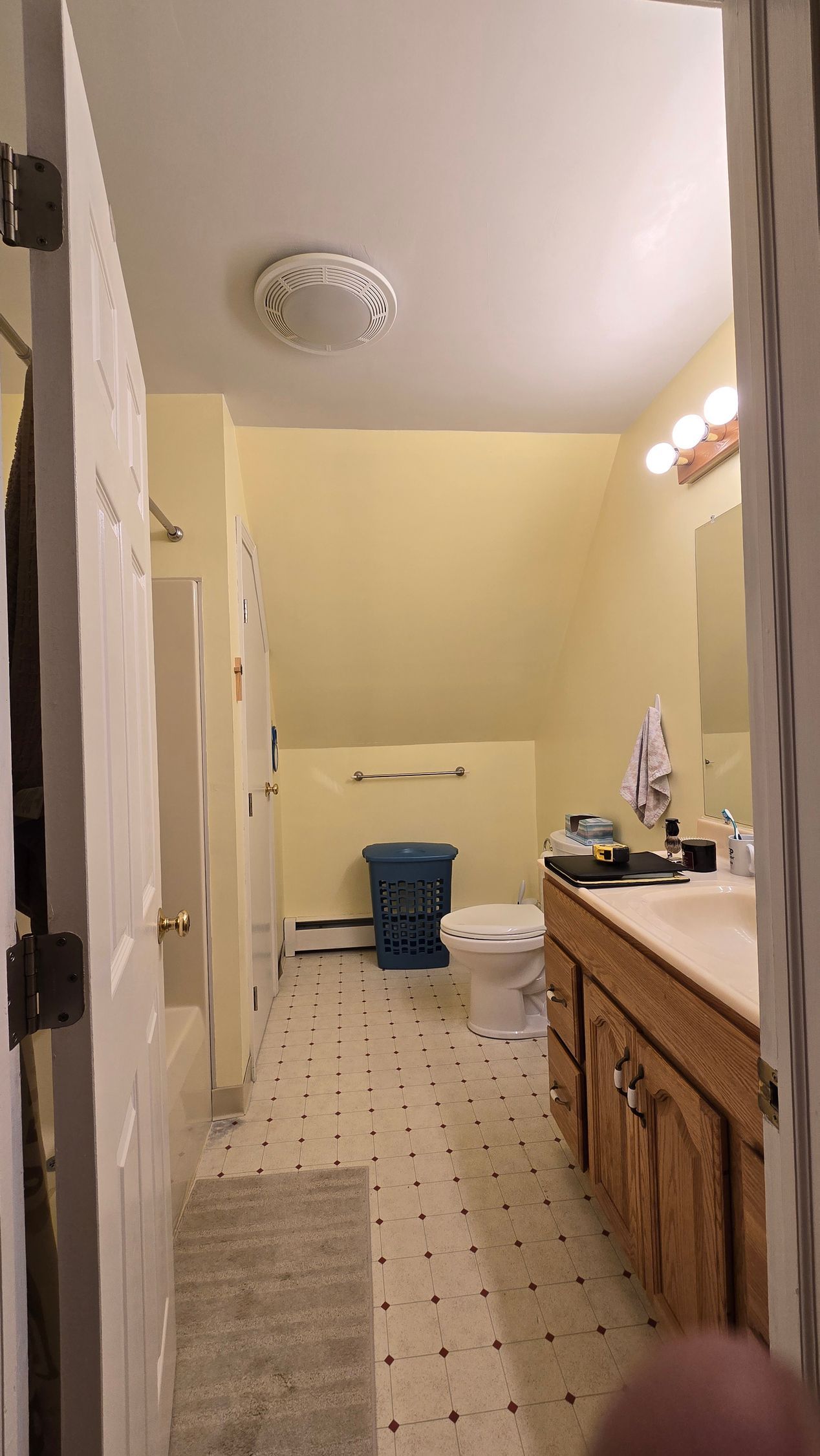 Narrow bathroom hallway with beige walls, wooden vanity, and a toilet in the back. By First Choice Bathroom Remodeling done in Plainville CT.