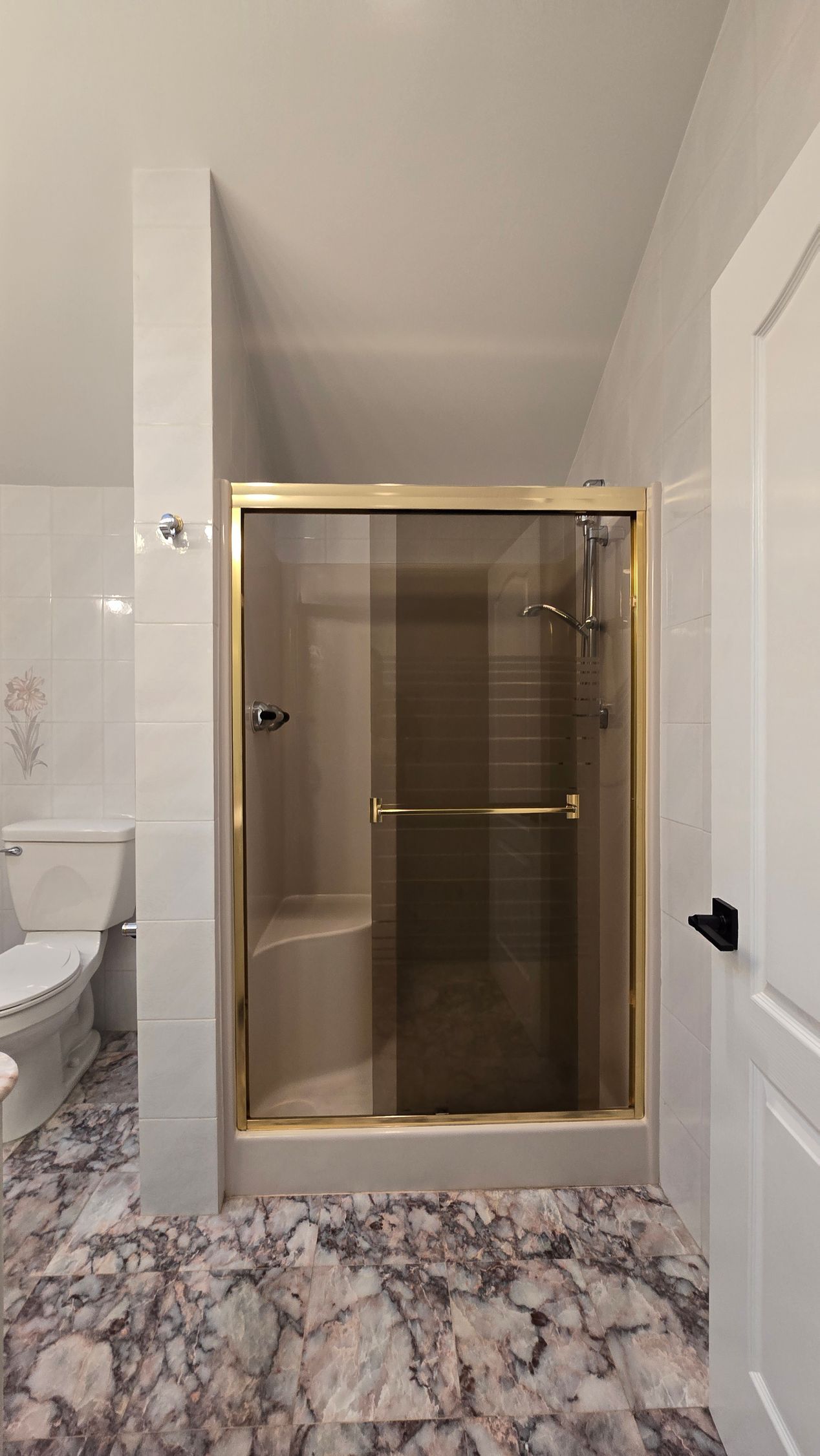 Bathroom with a gold-framed glass shower enclosure and marble-pattern floor tiles