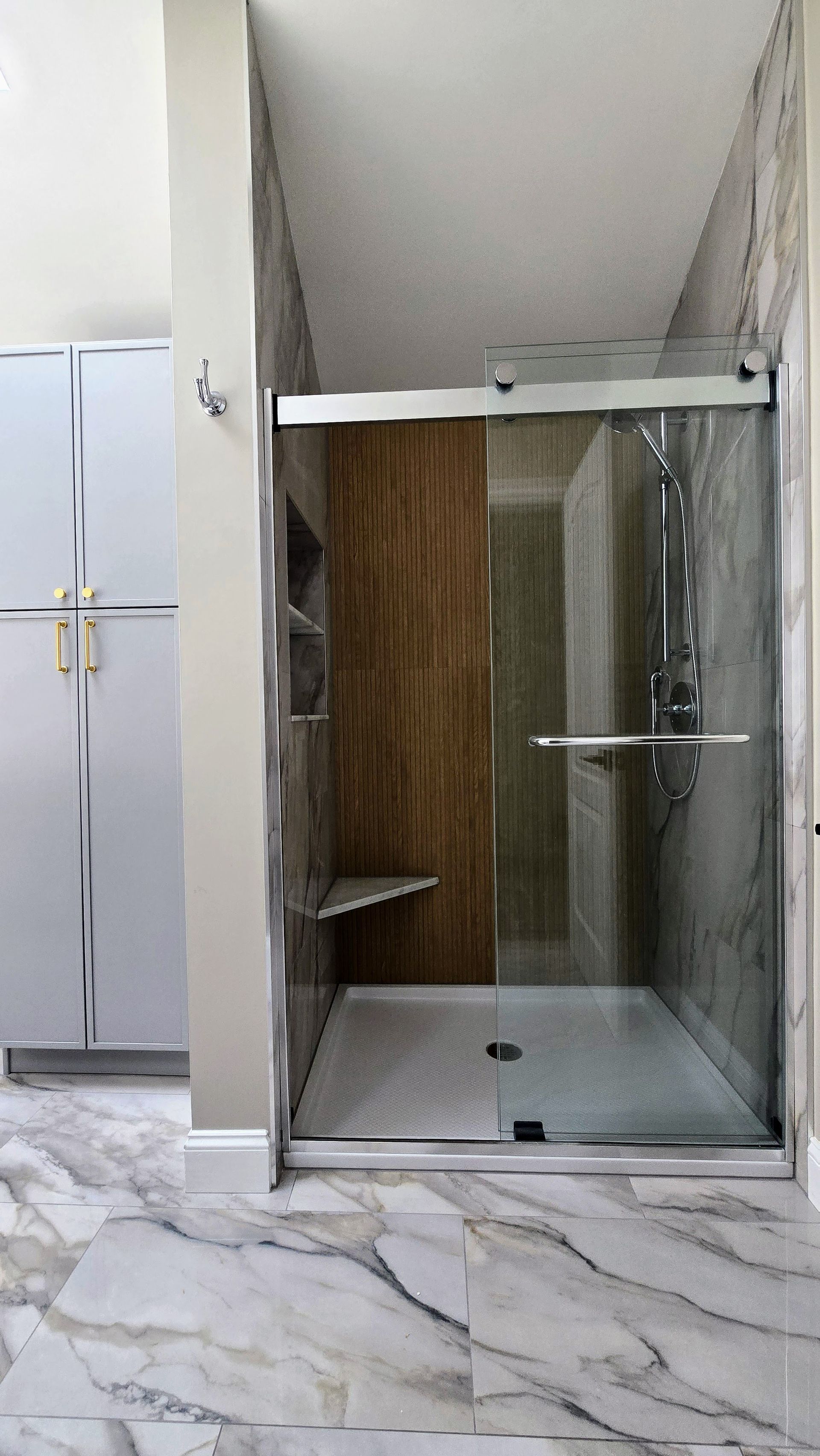 Glass walk-in shower with wood-look accent wall and marble-patterned bathroom floor