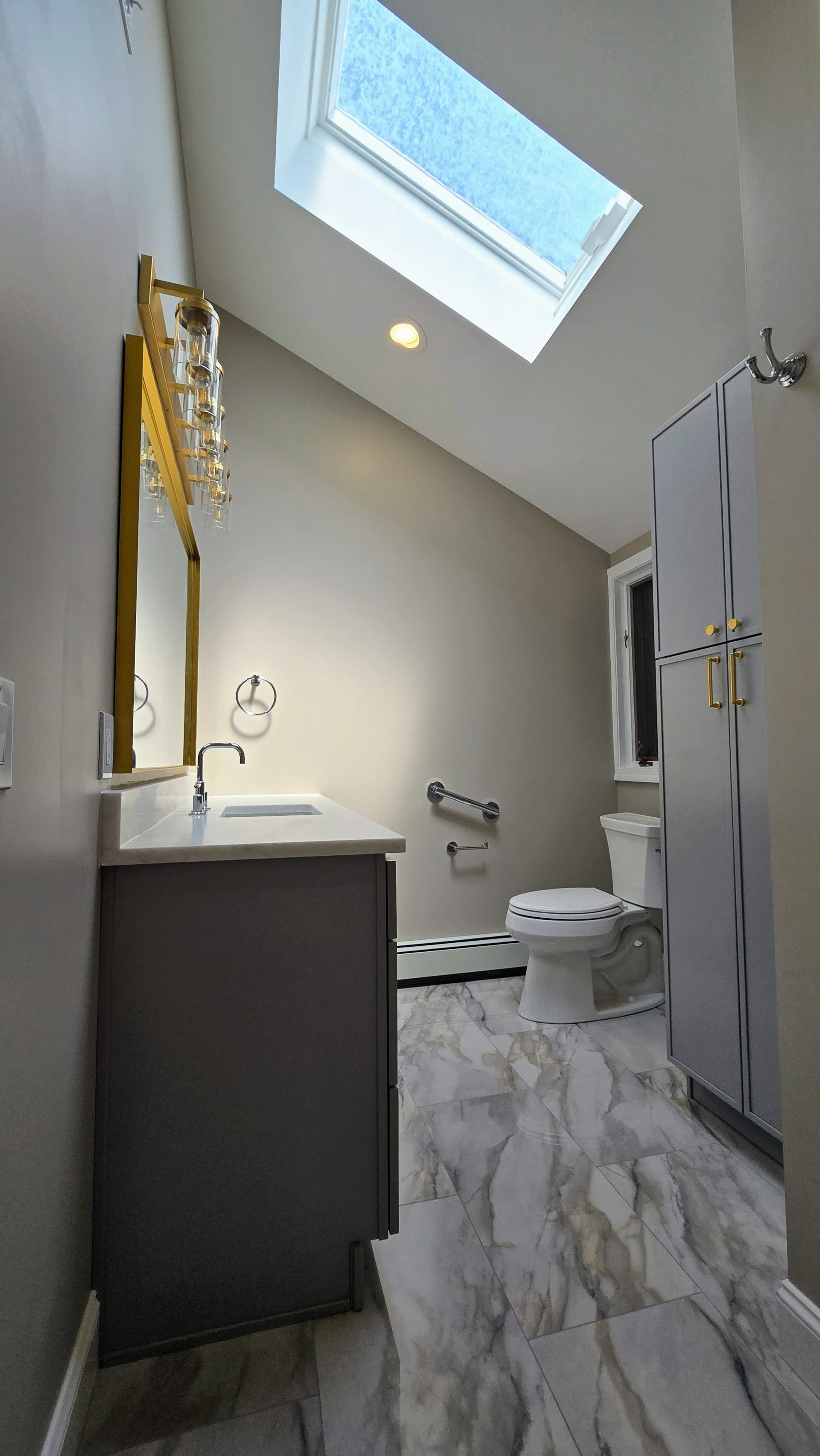 Narrow bathroom with skylight, white toilet, vanity, and marble-pattern floor tiles