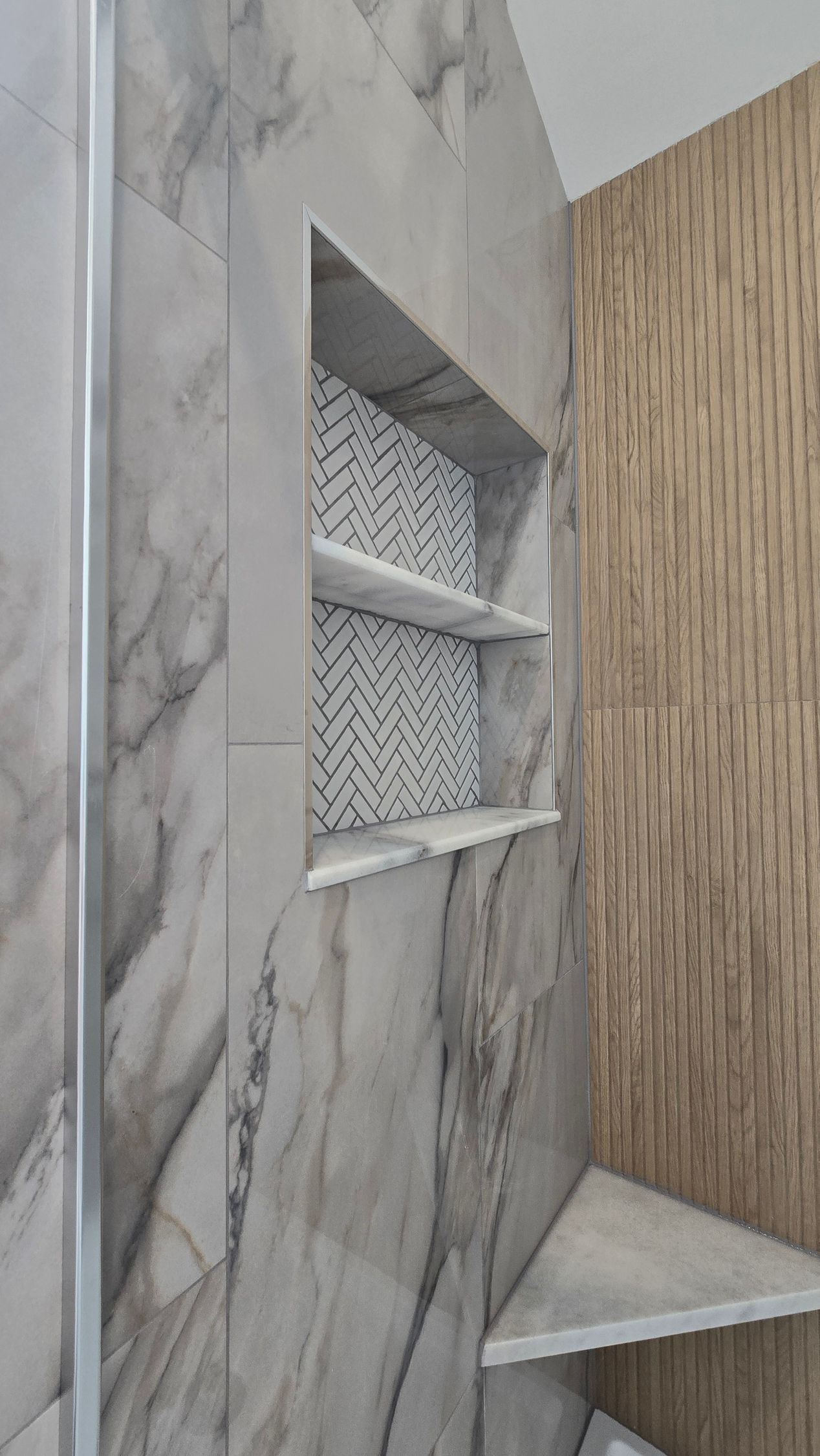 Modern shower with gray marble tile, woven niche shelves, and a small corner bench