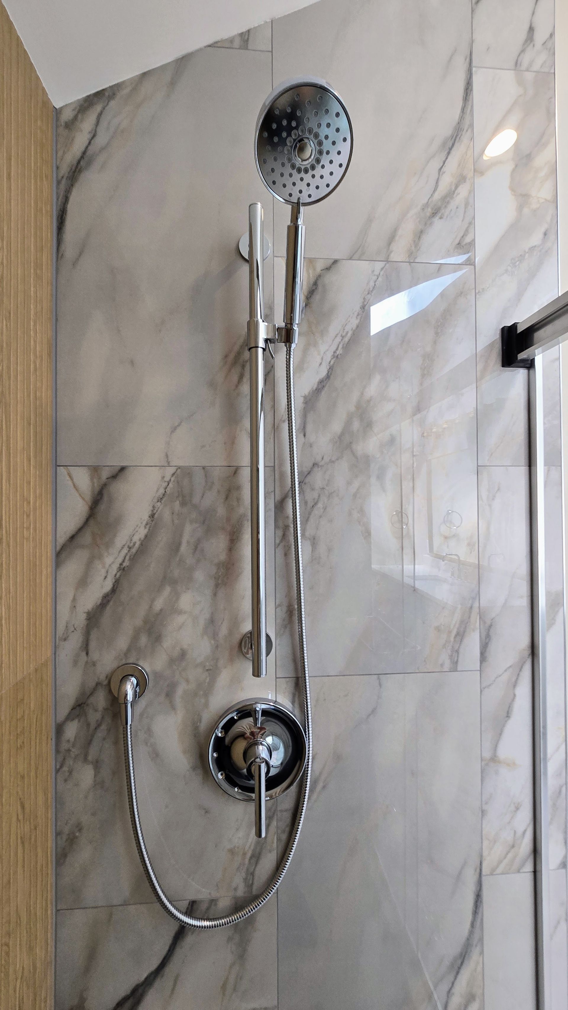 Chrome showerhead and handheld shower on a marble-tiled bathroom wall