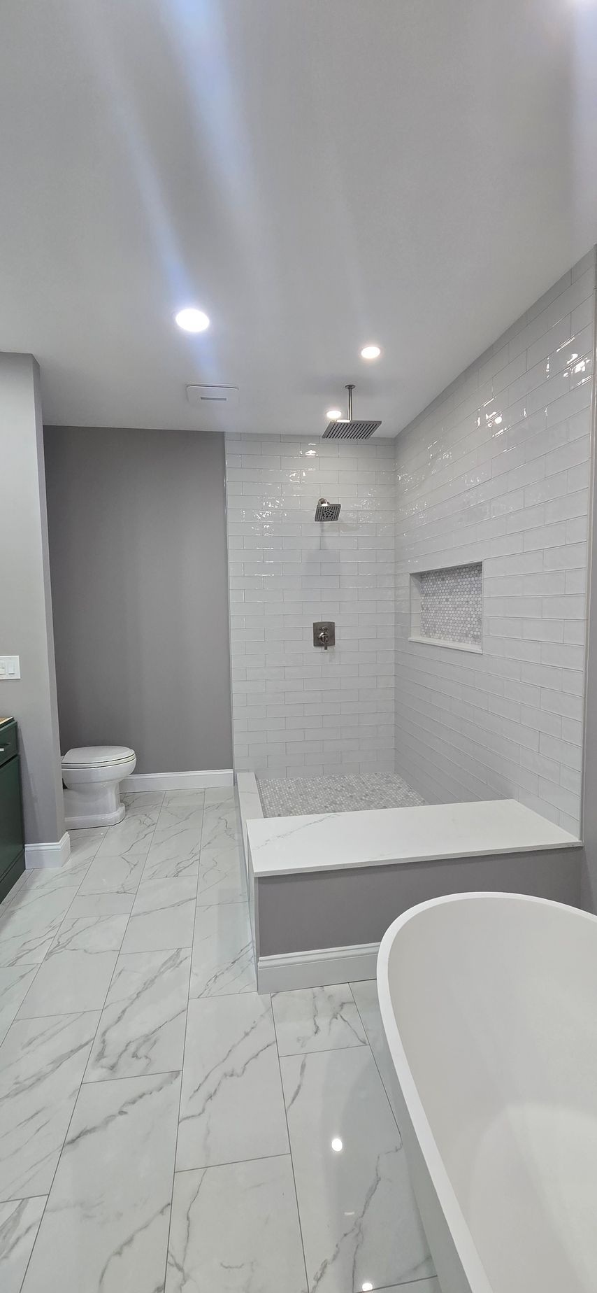 Modern white bathroom with glass shower, freestanding tub, and marble-look tile floor. By First Choice Bathroom Remodeling done in Haddam, CT.