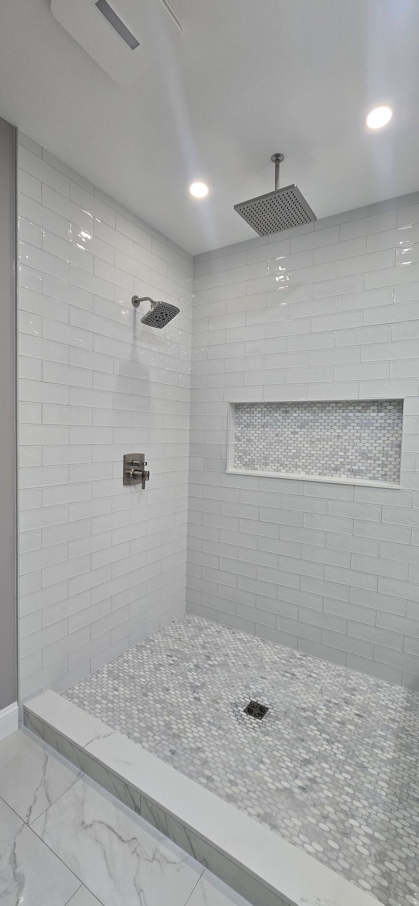 Modern tiled shower stall with rain showerhead, wall niche, and mosaic floor tiles. By First Choice Bathroom Remodeling done in Haddam, CT.