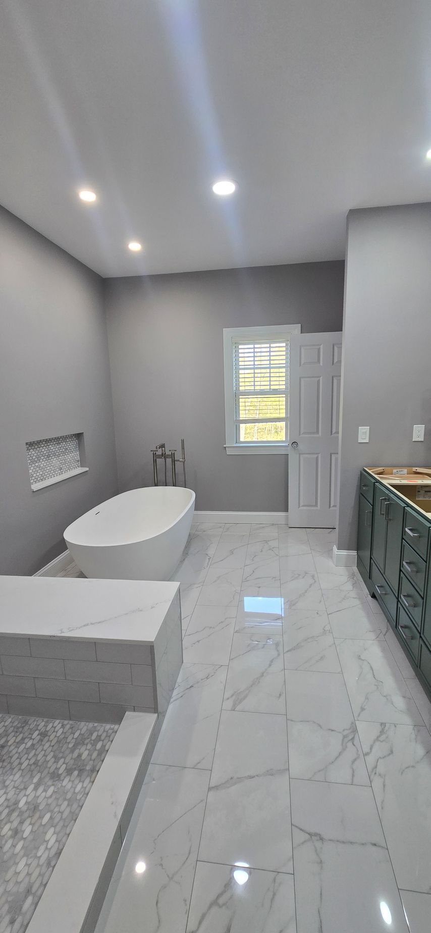 Modern bathroom with freestanding tub, gray tile floors, vanity, and bright recessed lighting