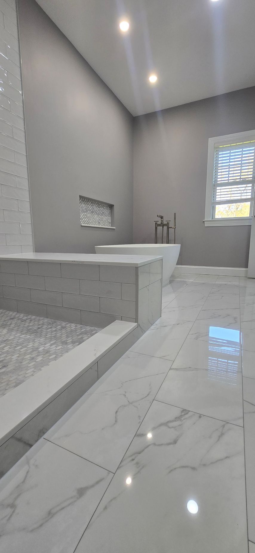 Modern gray tiled bathroom with a freestanding tub, large window, and walk-in shower. By First Choice Bathroom Remodeling done in Haddam, CT.