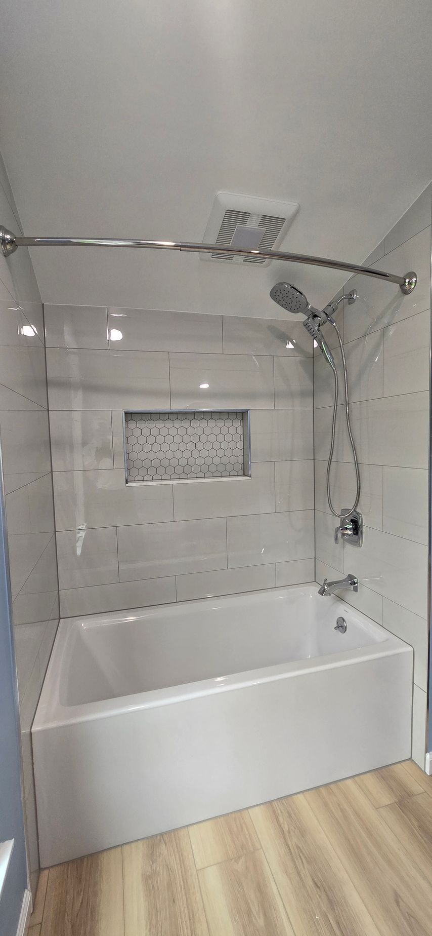 Modern white bathroom with a large bathtub, glass shower enclosure, and wood-look floor tiles.